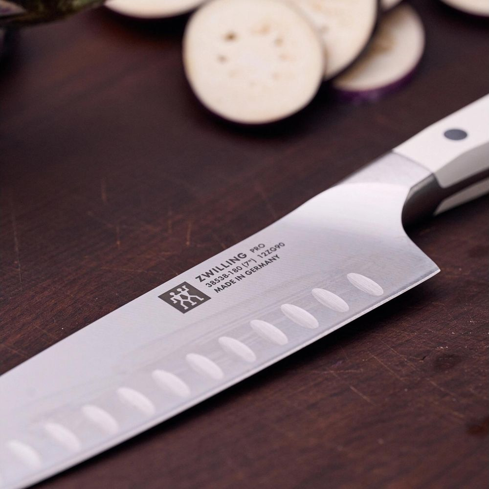 Ein ZWILLING Messer liegt auf einem Holzbrett neben aufgeschnittenen Auberginen.