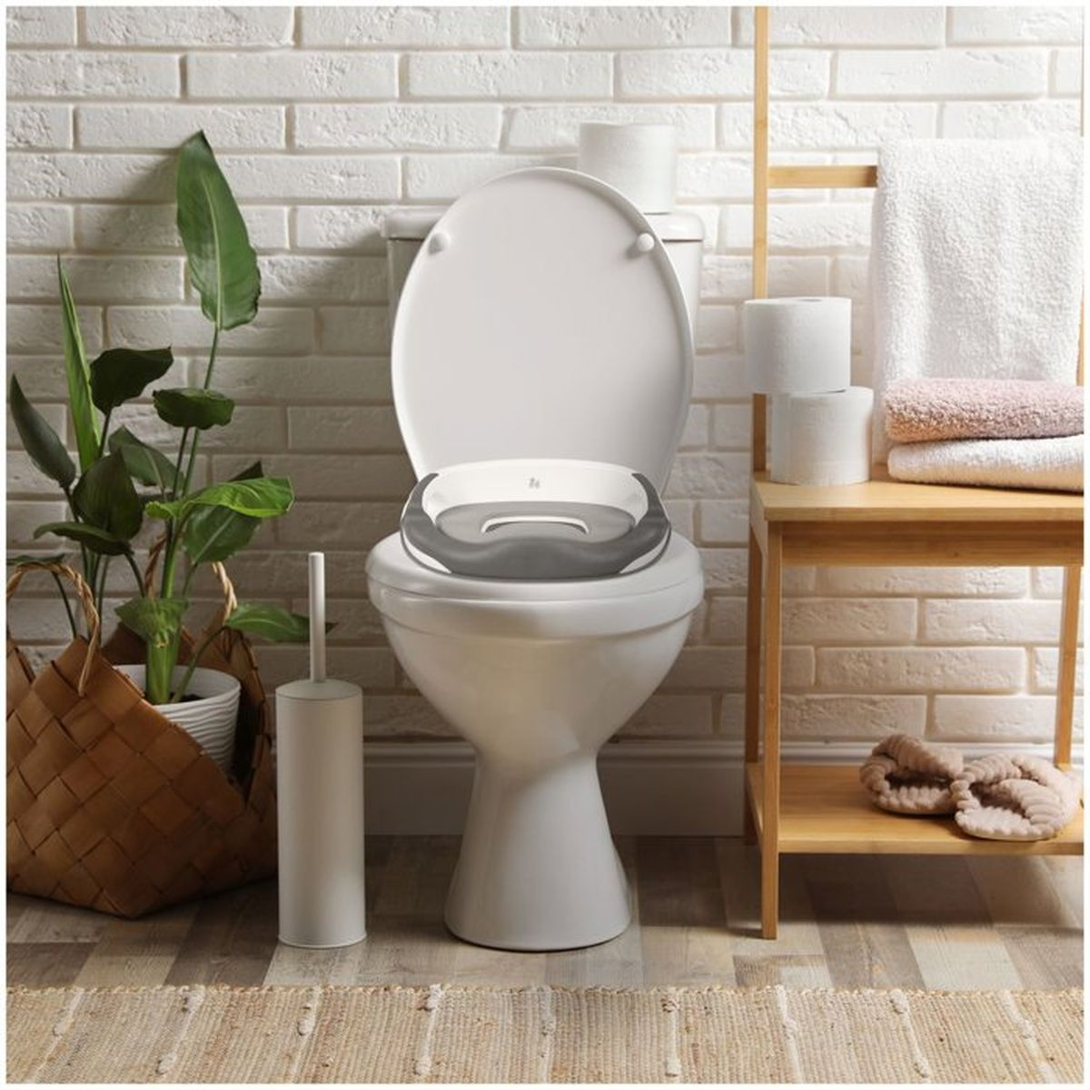 Ein weißer Toilettensitz mit Kindereinsatz steht vor einer Ziegelwand.