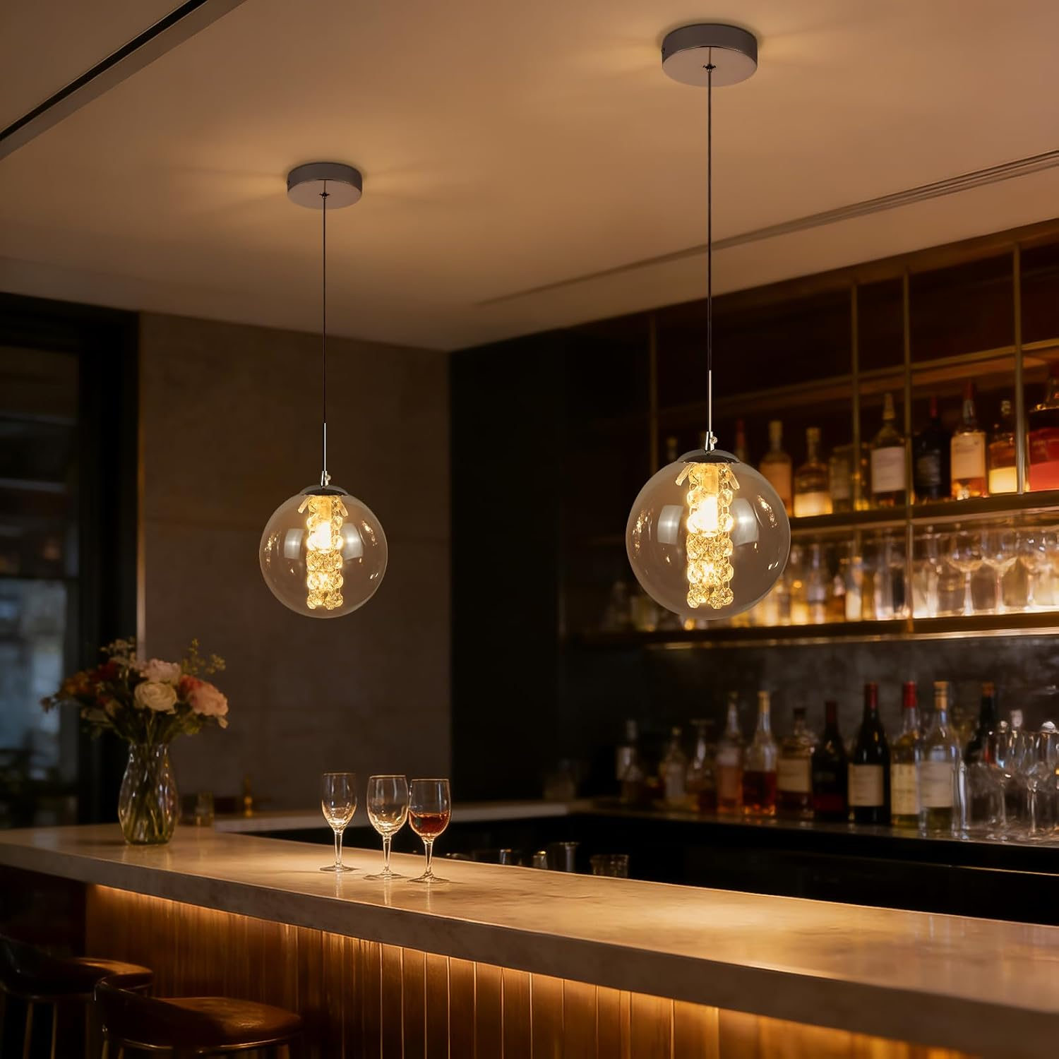 Due lampade a sospensione pendono sopra un bar con bicchieri e bottiglie sullo scaffale.