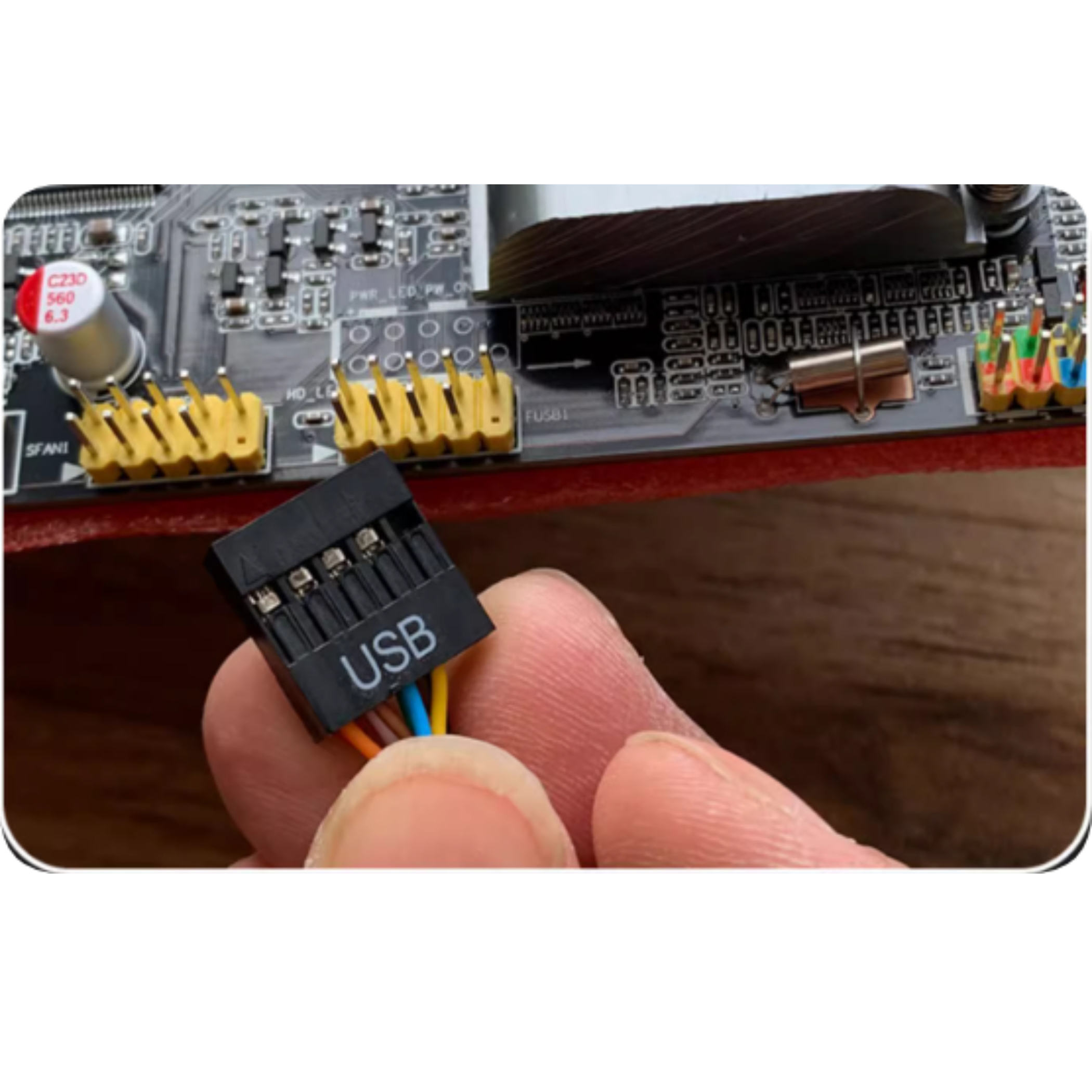 Ein Finger hält einen USB-Anschluss mit bunten Kabeln vor einer Computerplatine.