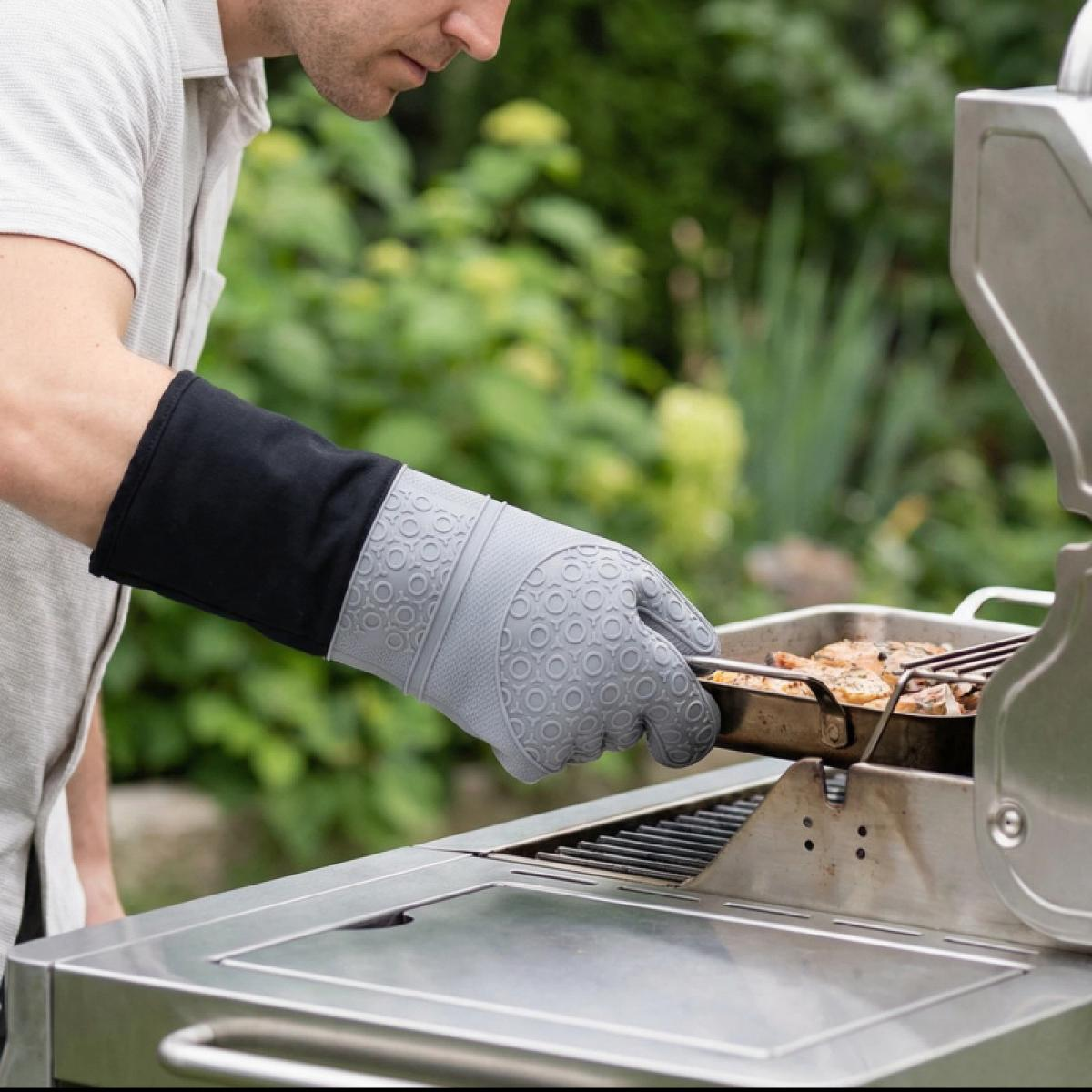 Mann in grauem Hemd grillt Essen in einer Pfanne mit einem grauen Ofenhandschuh.