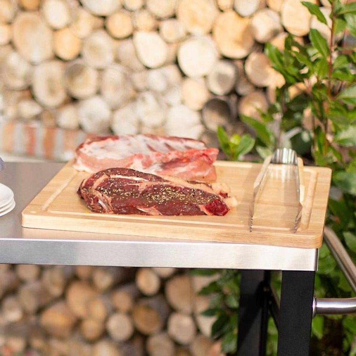Rohes Fleisch auf einem Holzbrett mit Gewürzen, daneben eine Grillzange.