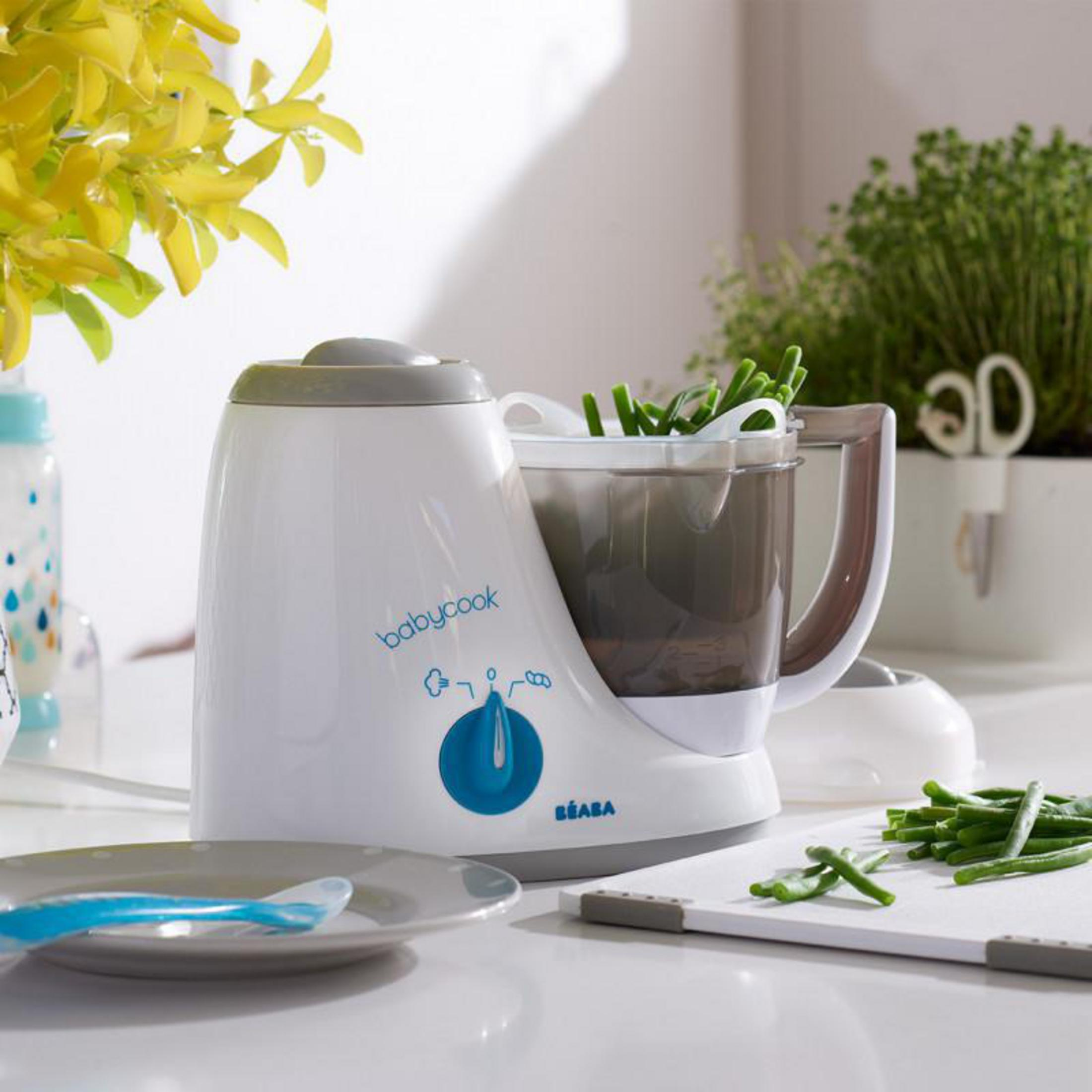Ein weißer Babycook-Mixer steht auf einer Arbeitsplatte mit grünen Bohnen.