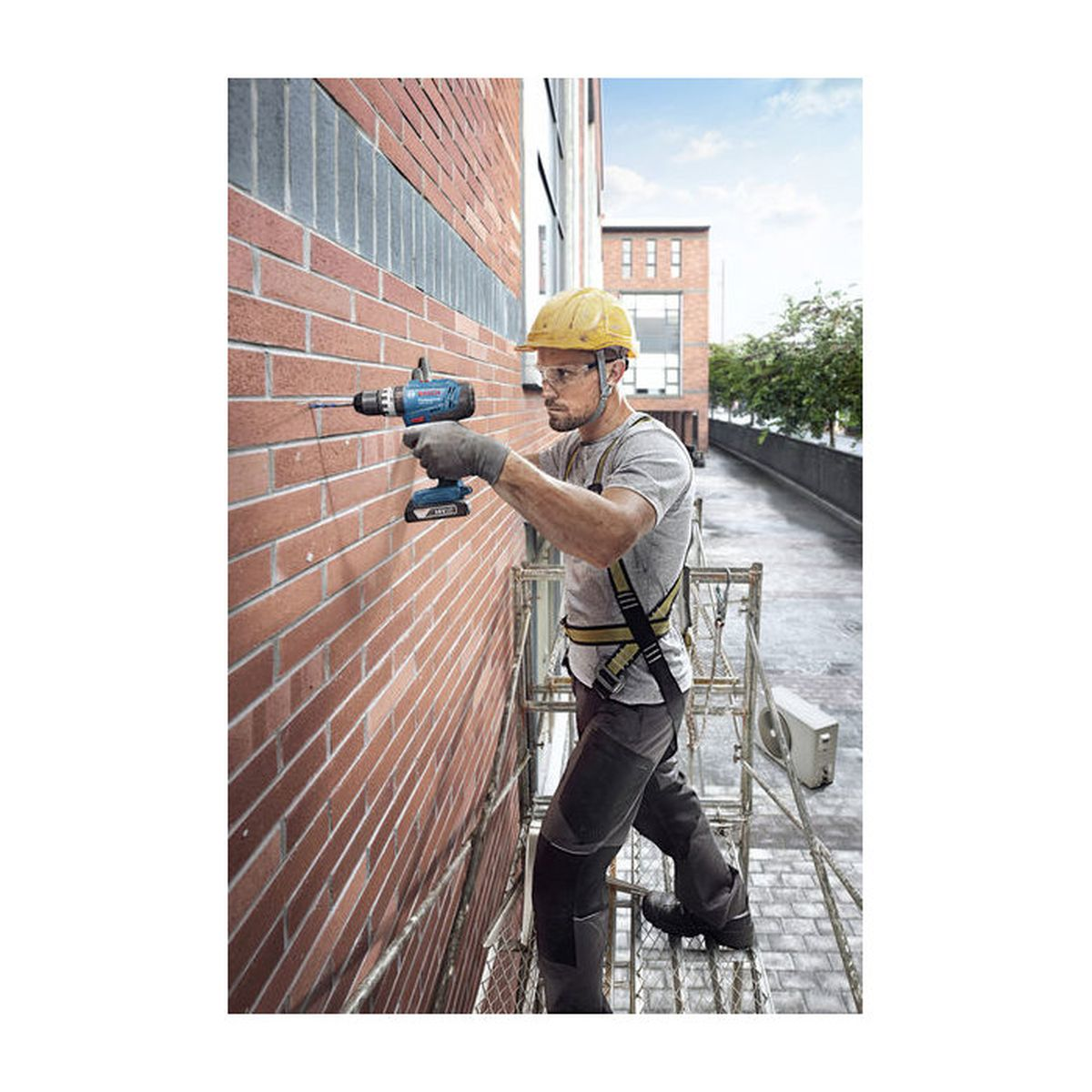 Mann mit Bohrmaschine bohrt in Ziegelwand von Gerüst.