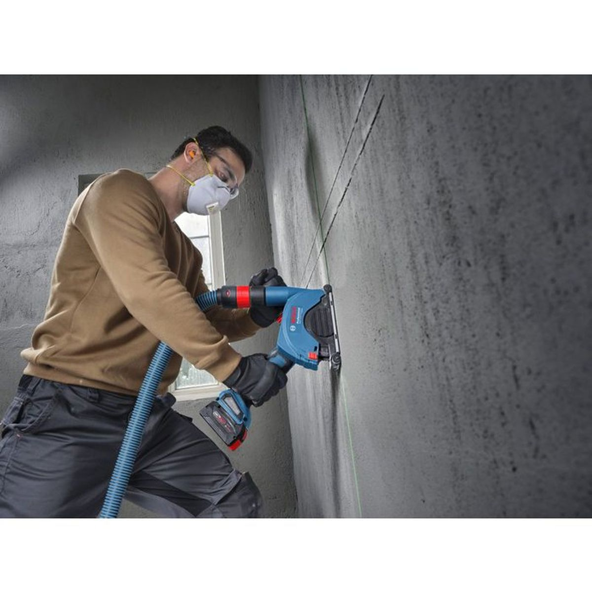 Mann mit Staubmaske schneidet Wand mit blauem Werkzeug, abgesaugt.