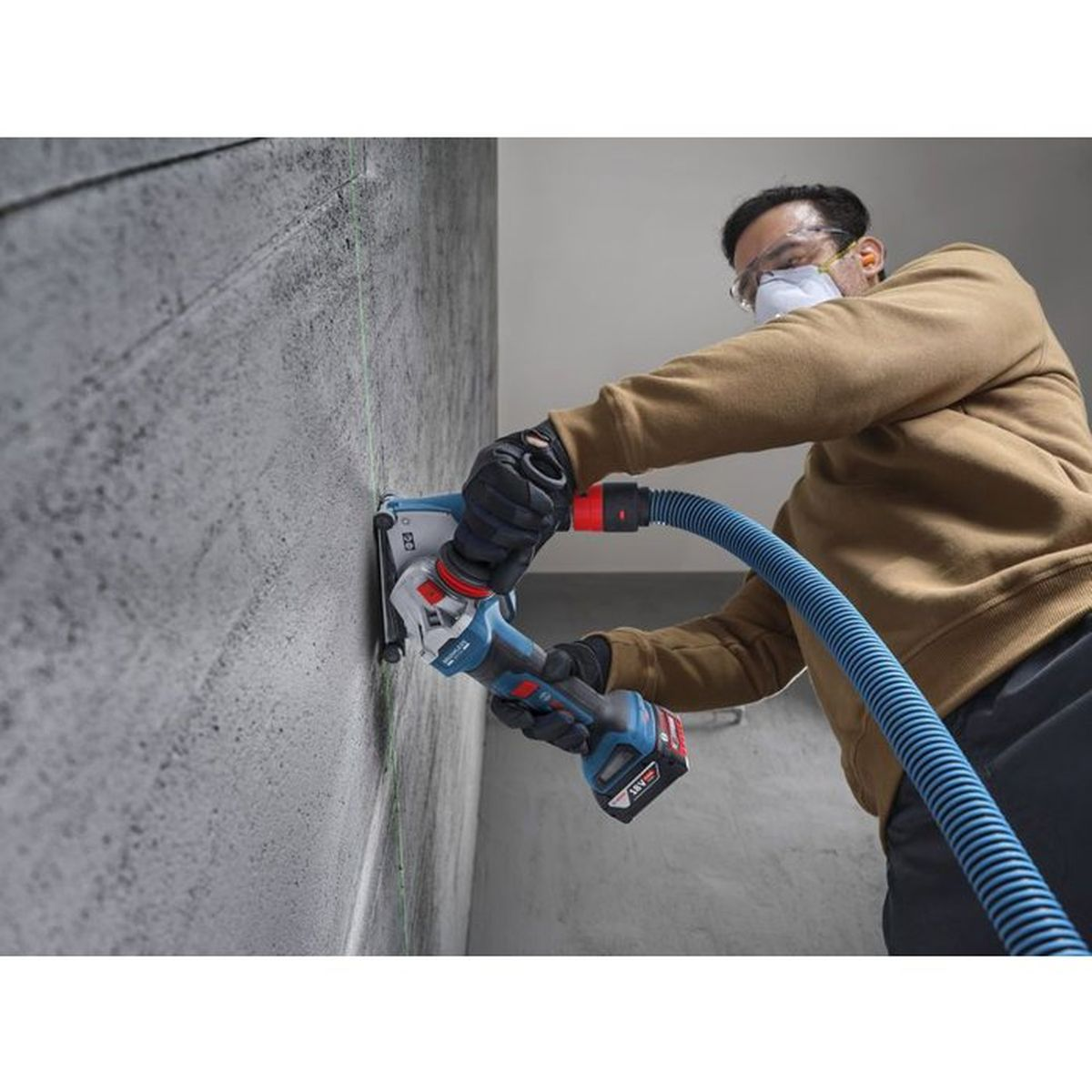 Mann schneidet Betonwand mit Schleifmaschine und Staubabsaugung. Schutzausrüstung getragen.