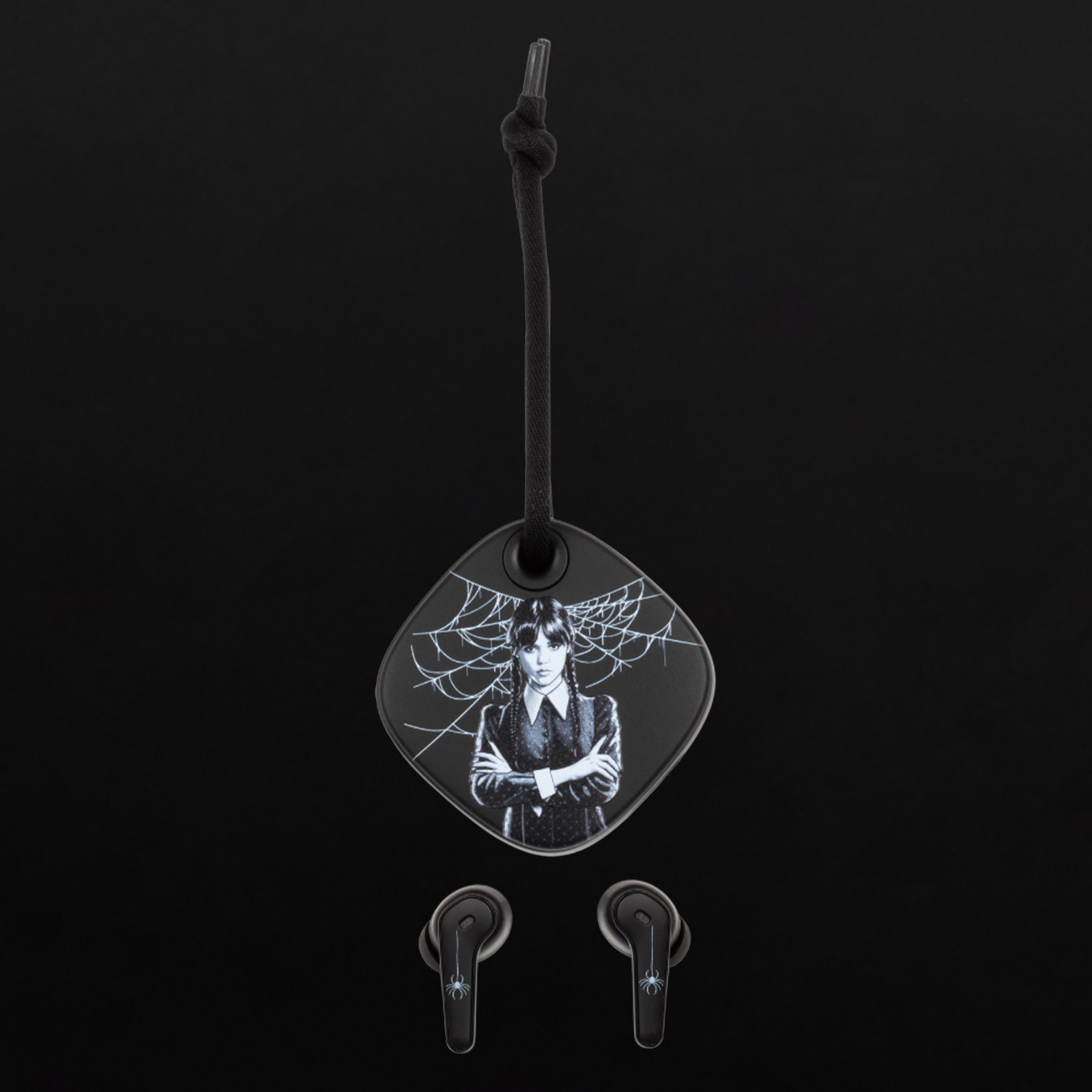 Brelok z Wednesday Addams i pajęczyną, obok dwóch słuchawek.