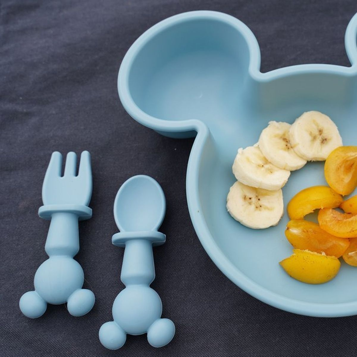 Hellblaues Mickey-Maus-Geschirr mit Bananenscheiben und Aprikosenstücken.