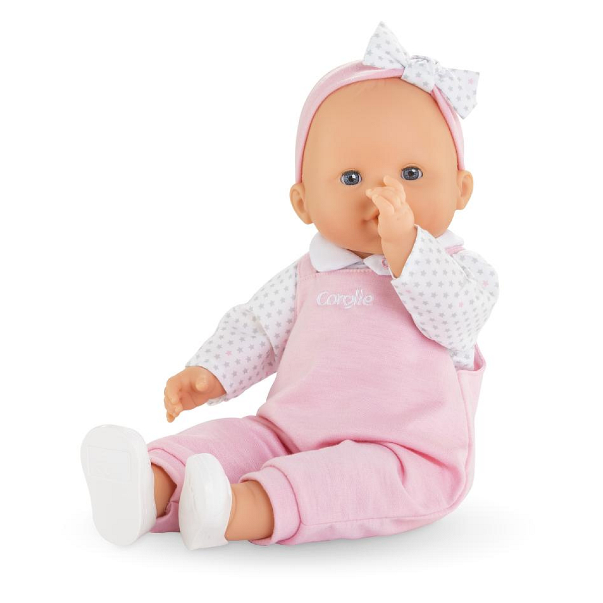Eine Puppe sitzt und steckt sich einen Finger in die Nase. Sie trägt rosa Latzhosen.