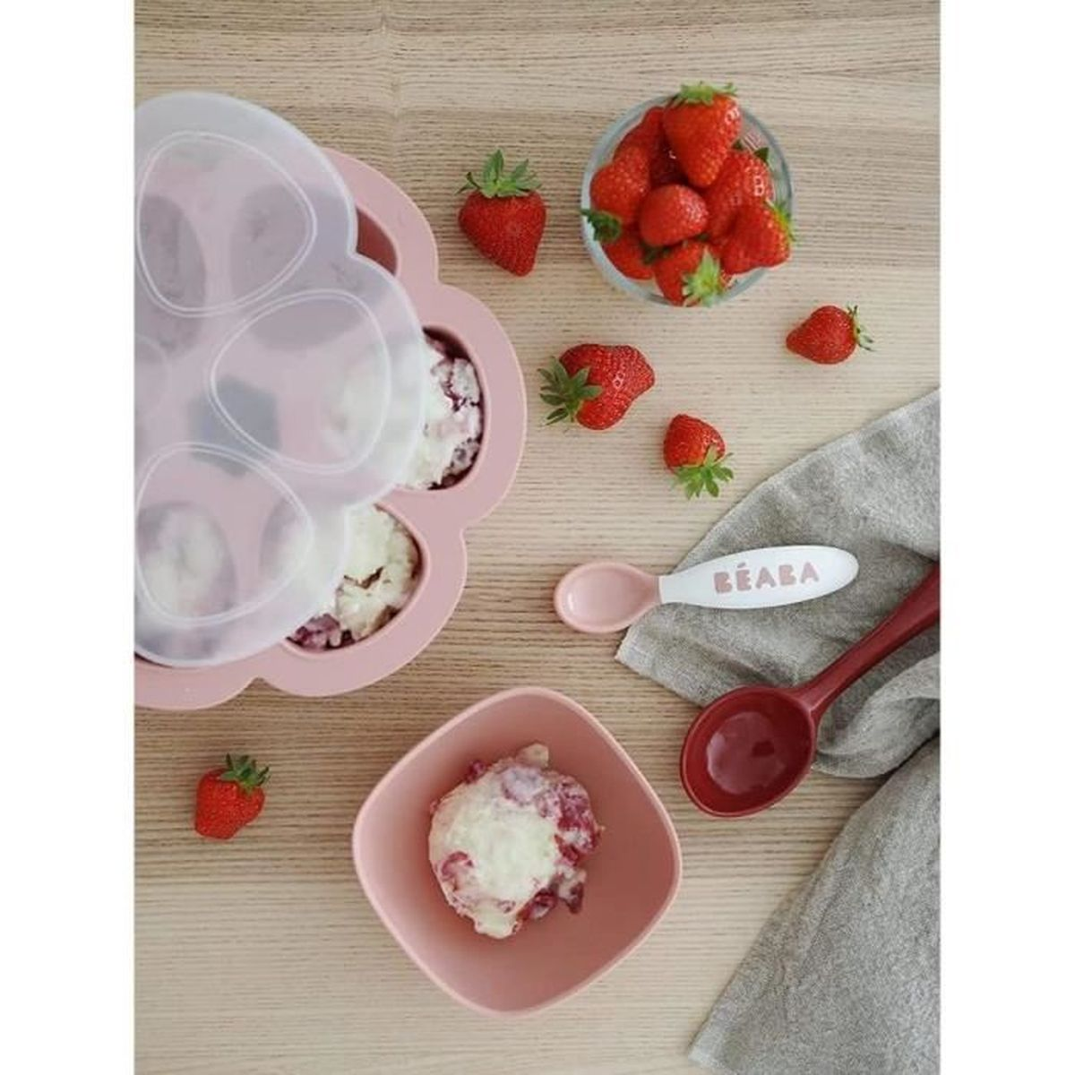 Rosa Eiswürfelform mit Erdbeeren, Schüssel und Löffeln auf Holzhintergrund.
