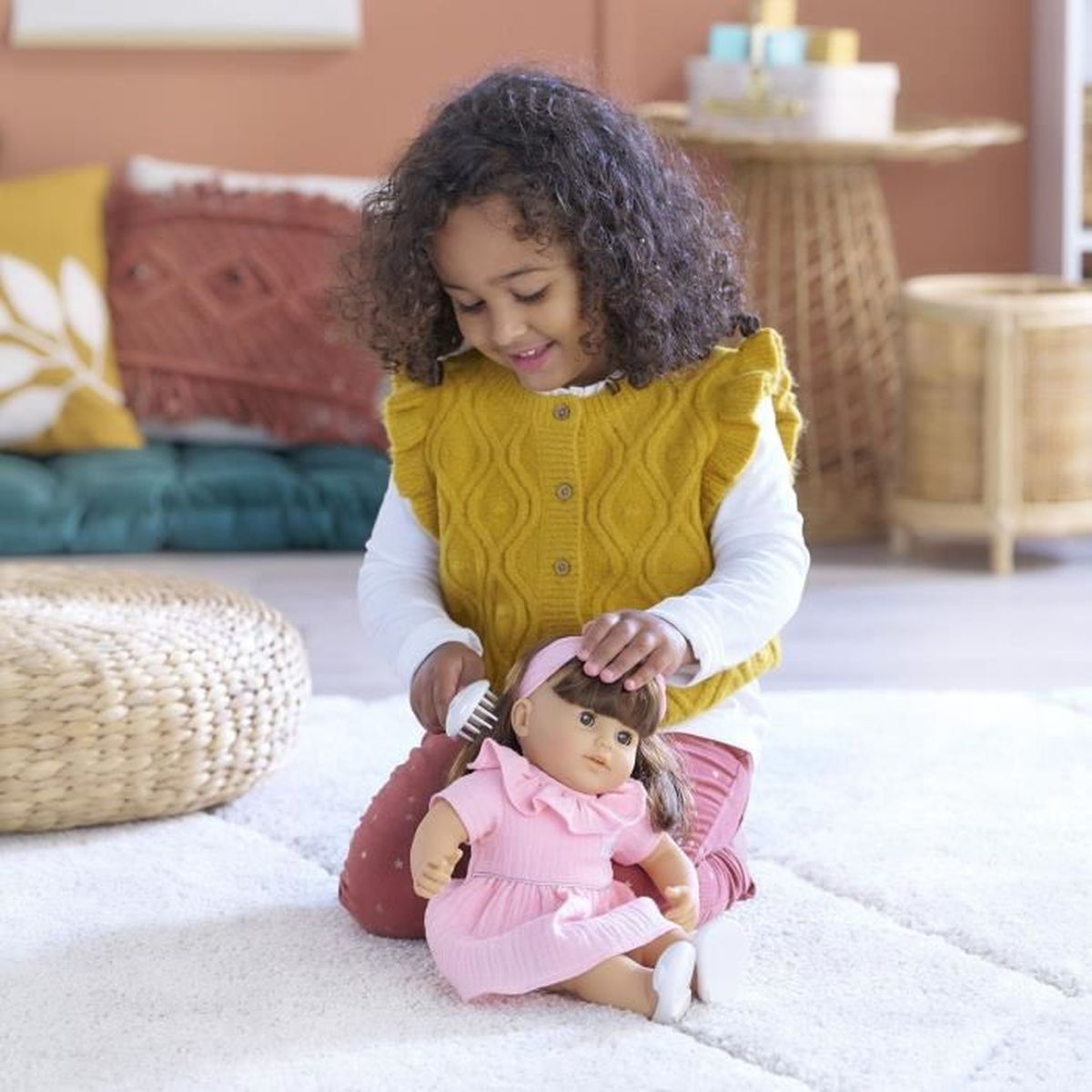Ein kleines Mädchen mit Locken bürstet eine Puppe in einem rosa Kleid.