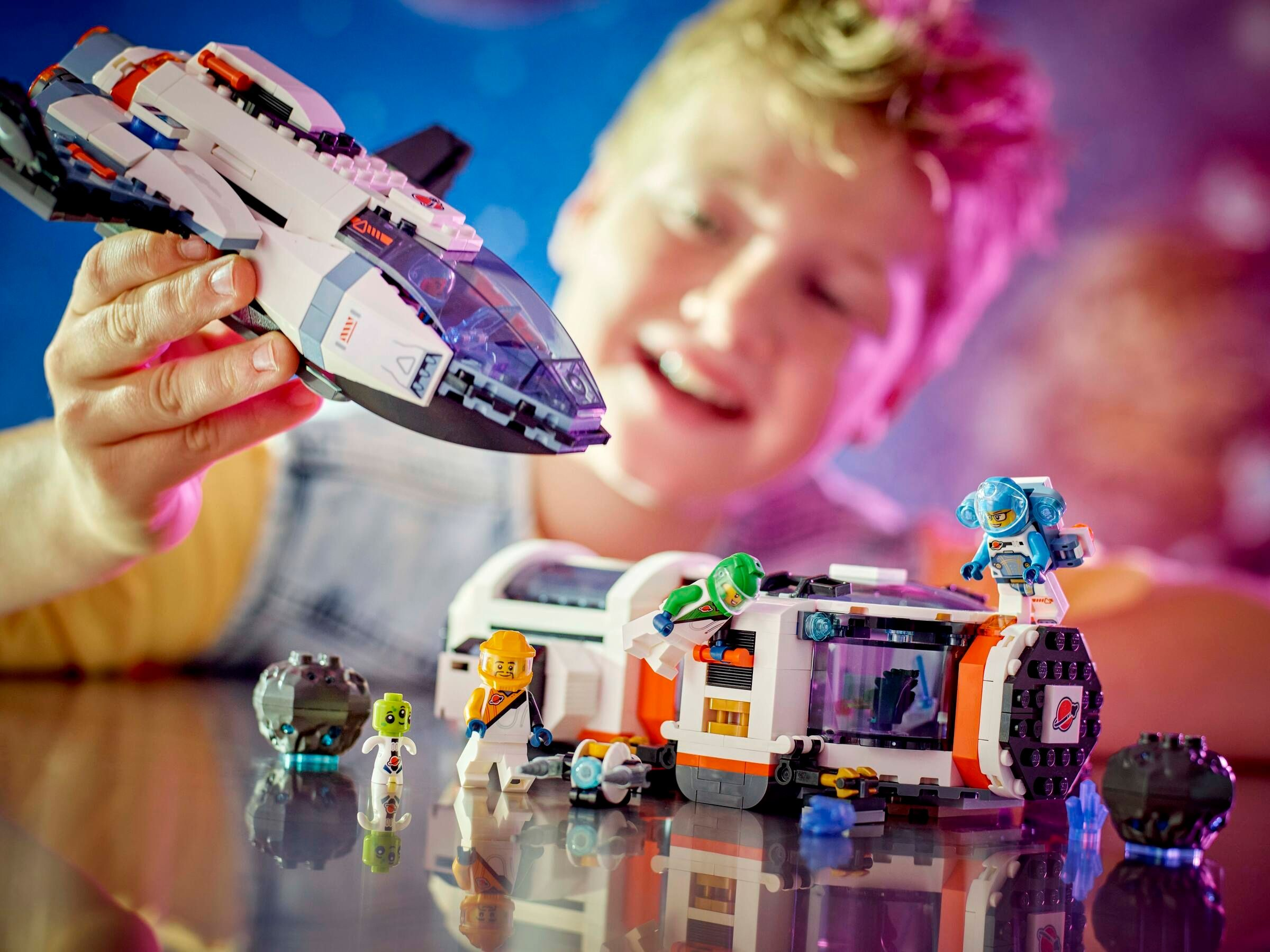 Ein Junge spielt mit Lego-Raumschiff und Figuren vor blauem Hintergrund.