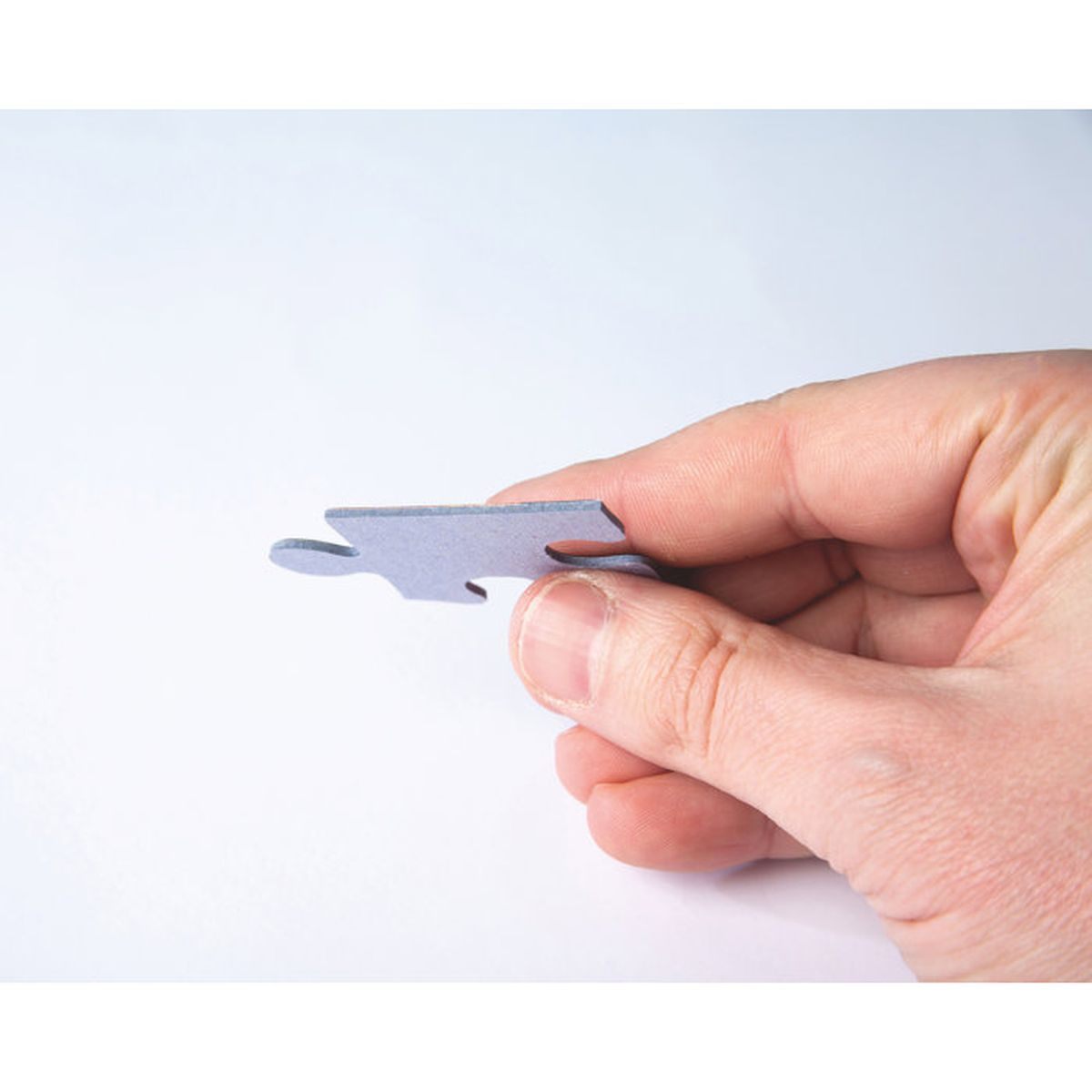Una mano tiene un pezzo di puzzle grigio con una linguetta e un'indentatura.