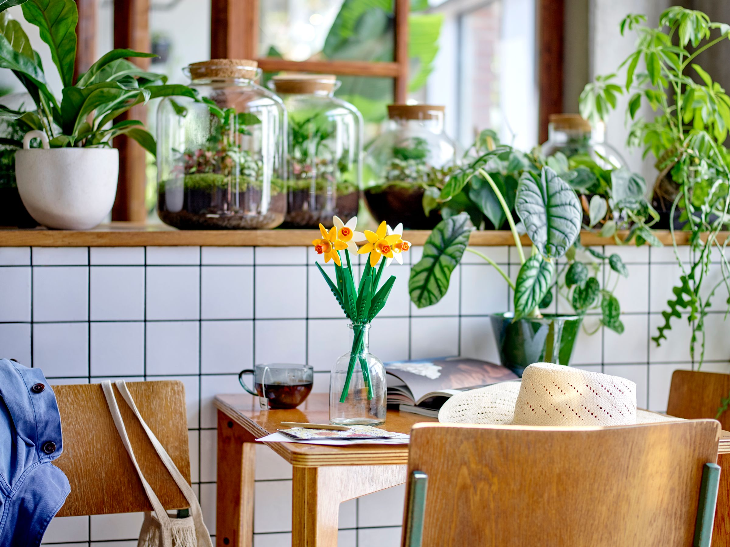 Gelbe und weiße Narzissen in einer Vase auf einem Holztisch mit Terrarien und Pflanzen.