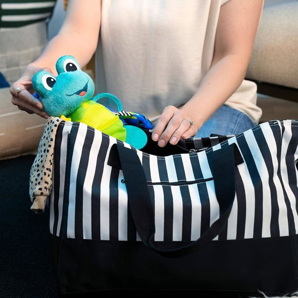 Eine Person packt eine blaue Froschspielzeug in eine gestreifte Tasche.