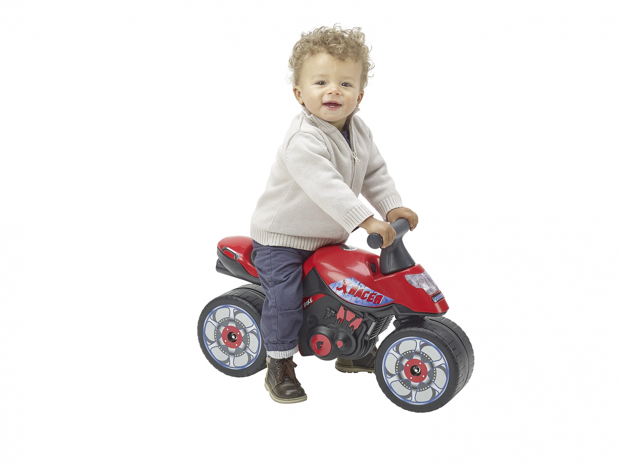 Un bambino piccolo con i capelli ricci siede su una moto giocattolo rossa su sfondo bianco.