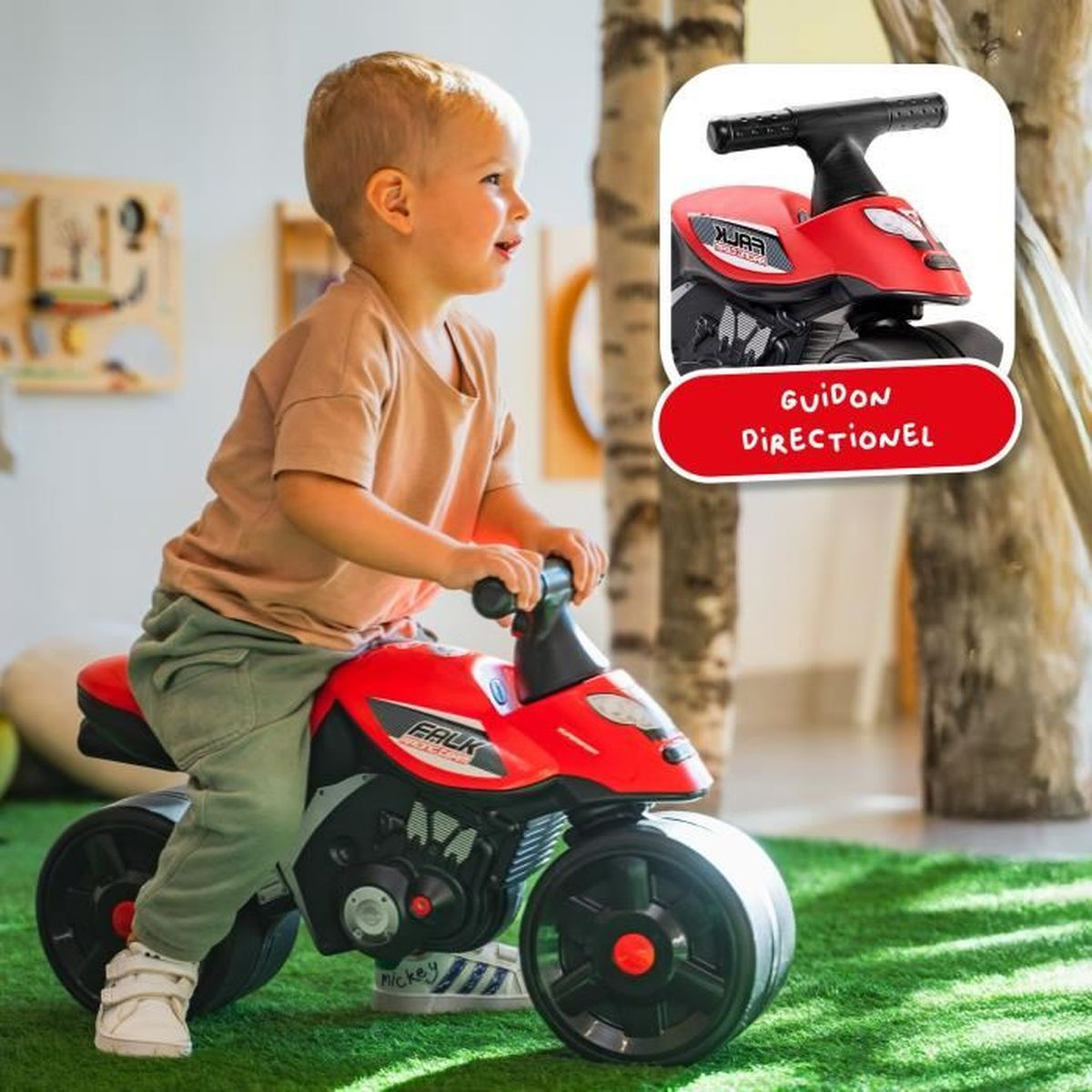 Un bambino cavalca una moto giocattolo rossa su un tappeto verde.