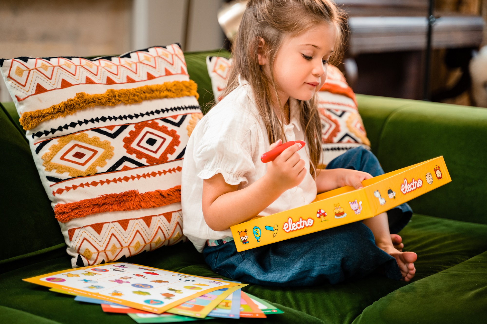 Una niña se sienta en un sofá verde, jugando con un juego.
