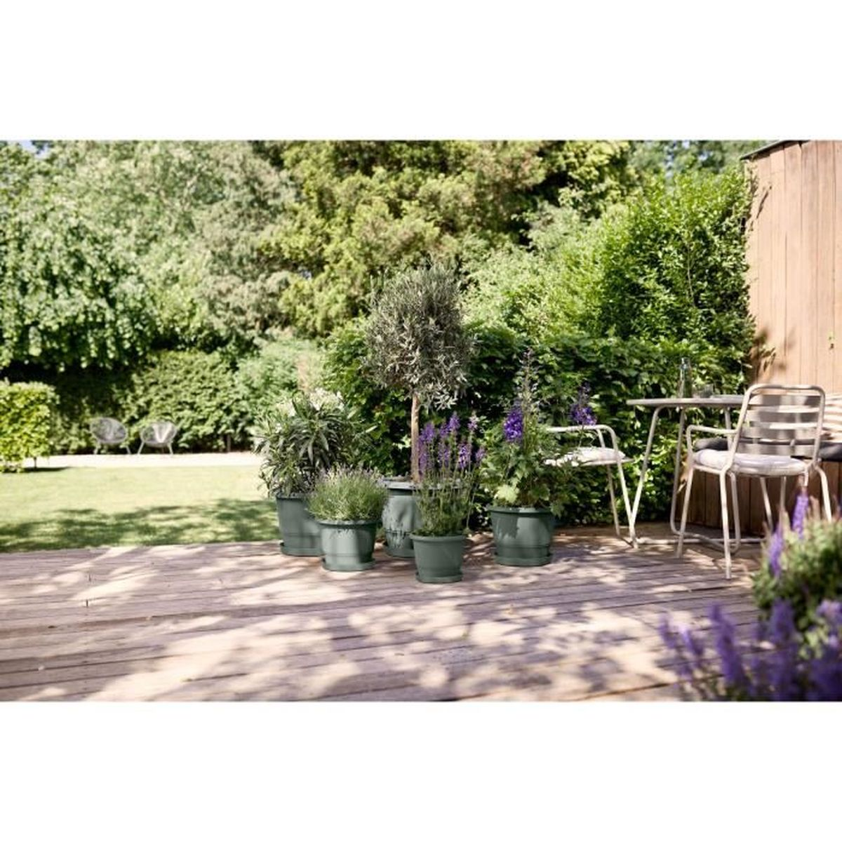 Ein Garten mit Holzdeck, Pflanzen in Töpfen und Sitzmöbeln.