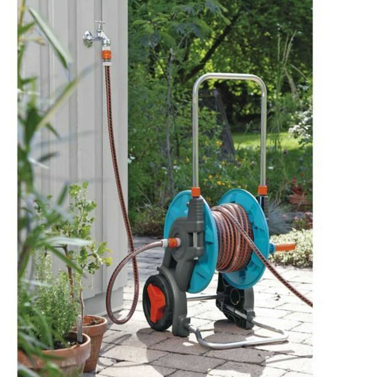 Ein Gartenschlauchwagen mit türkisfarbenen Spulen steht auf einer gepflasterten Fläche.