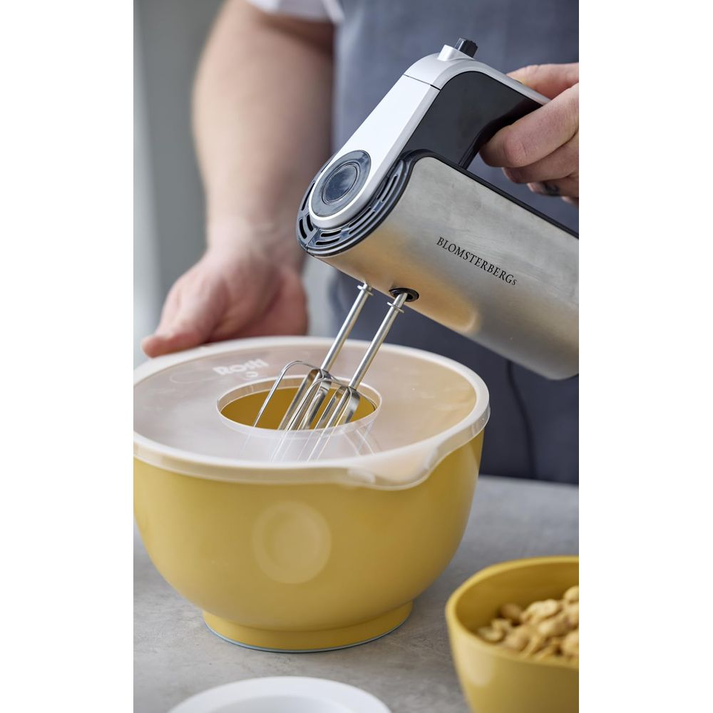 Ein Handmixer aus Metall und Schwarz wird in eine gelbe Schüssel gehalten.