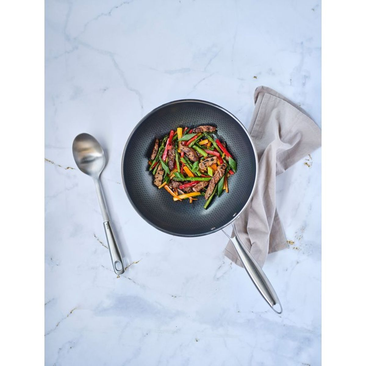 Ein Wok gefüllt mit Rindergeschnetzeltem, Spargel und Paprika auf Marmor.