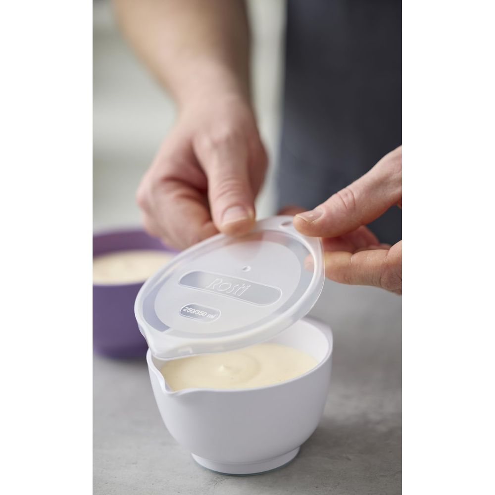Hände halten einen transparenten Deckel über einer weißen Schüssel mit gelber Creme.