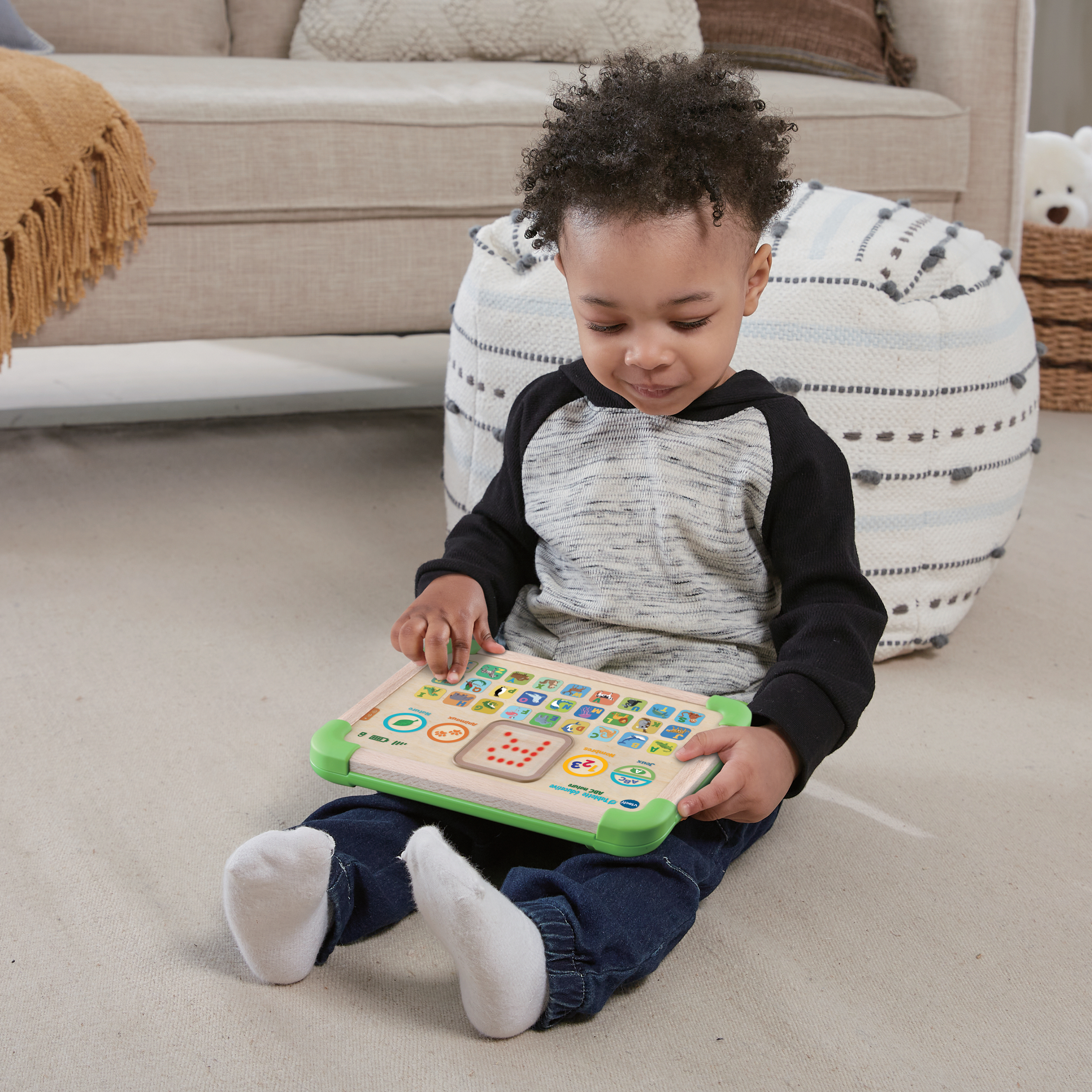 Un jeune enfant joue avec une tablette jouet interactive sur le sol.