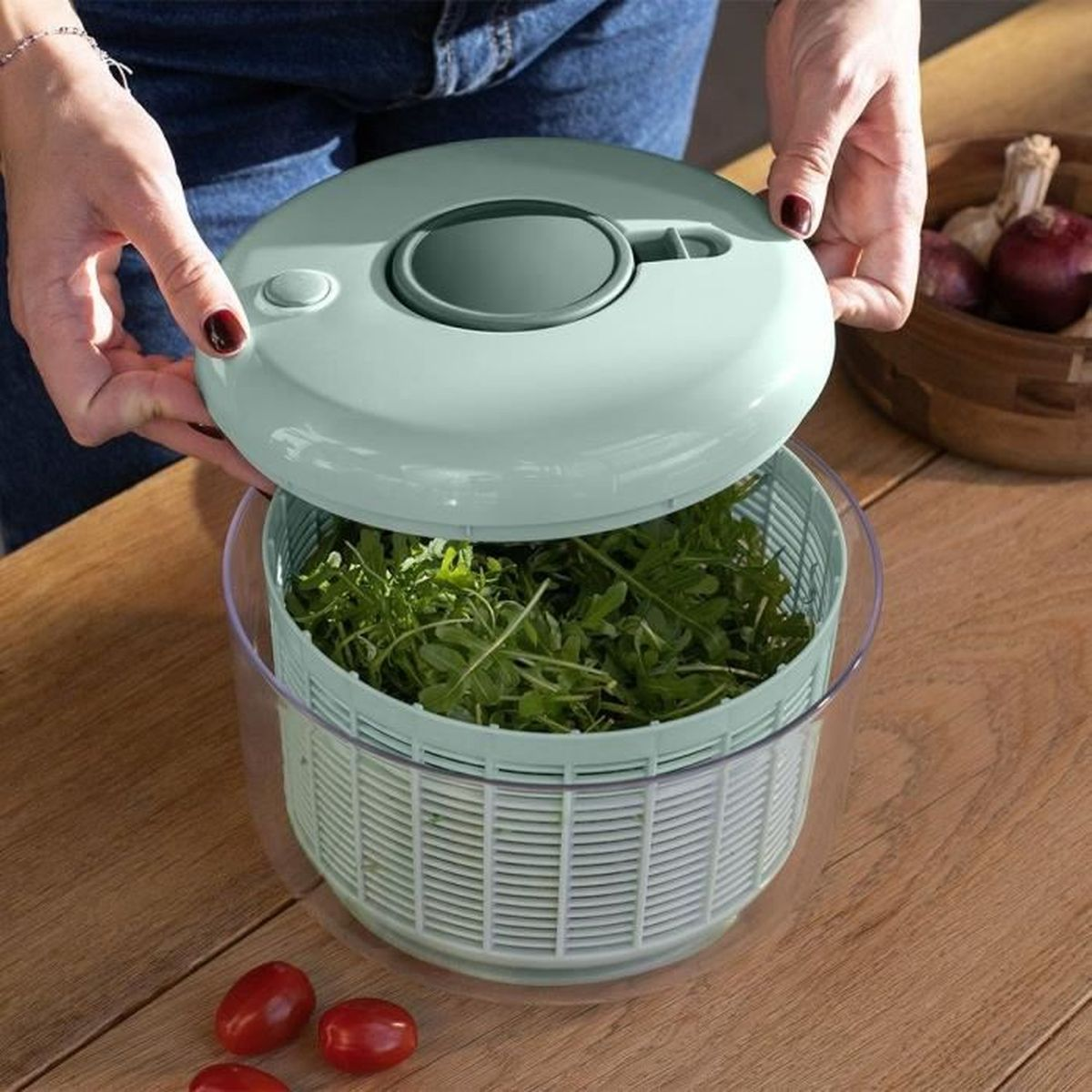Eine Person öffnet einen Salat-Schleuderer mit grünem Salat und Tomaten.
