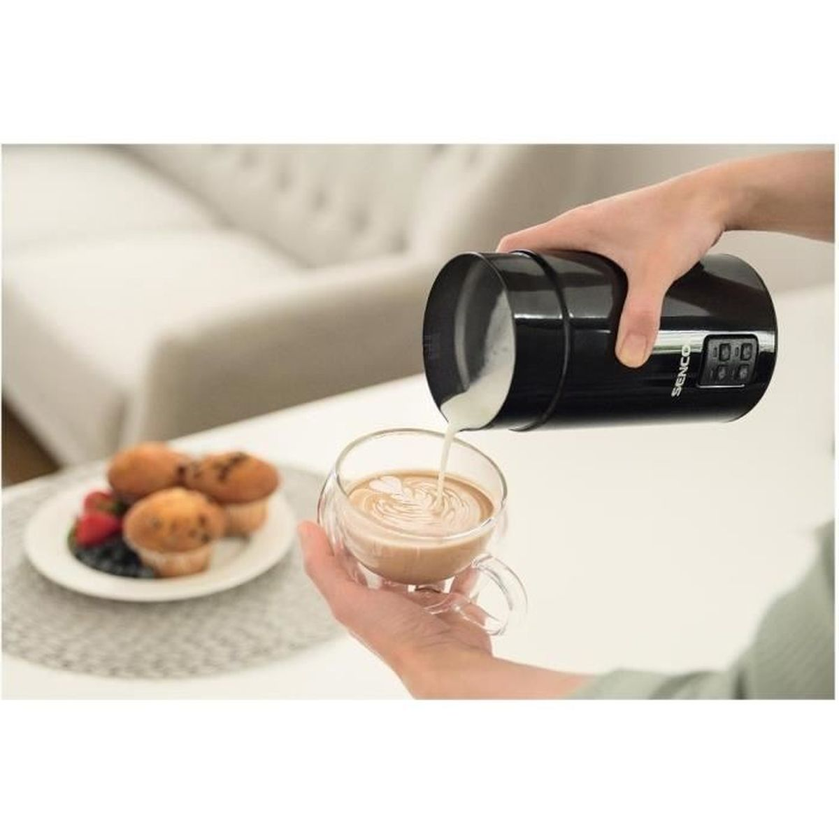 Milch wird aus einem schwarzen Behälter in eine Glas Tasse mit Kaffee gegossen.