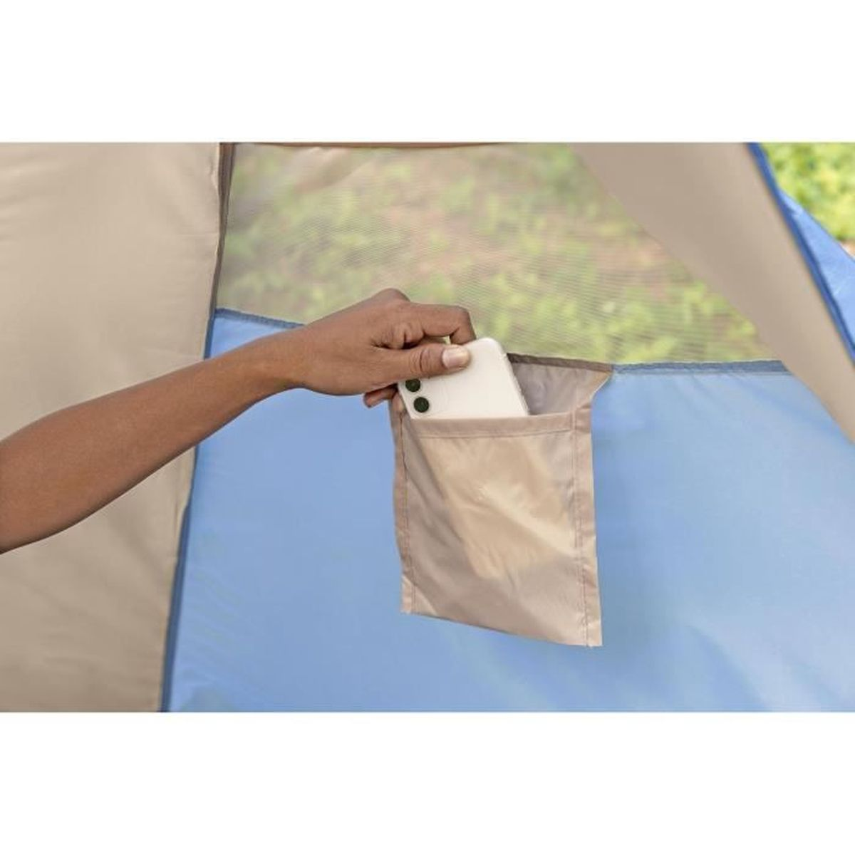 Eine Hand steckt ein weißes Smartphone in eine beige Tasche an einer blauen Zeltwand.