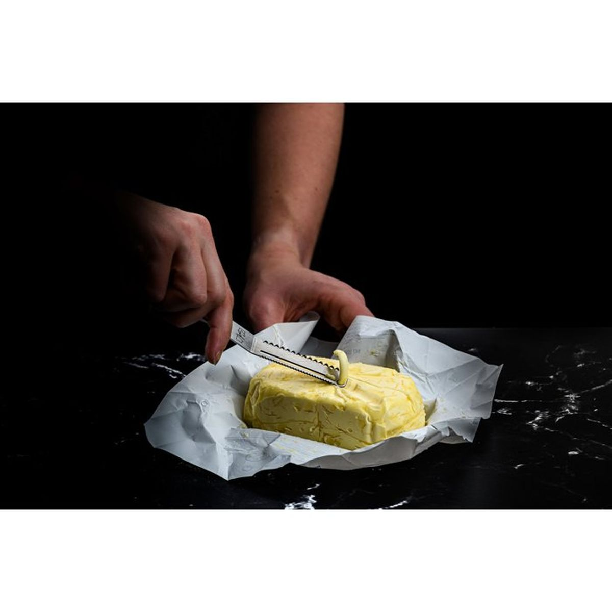 Una persona corta un bloque de mantequilla con un cuchillo para queso sobre mármol.