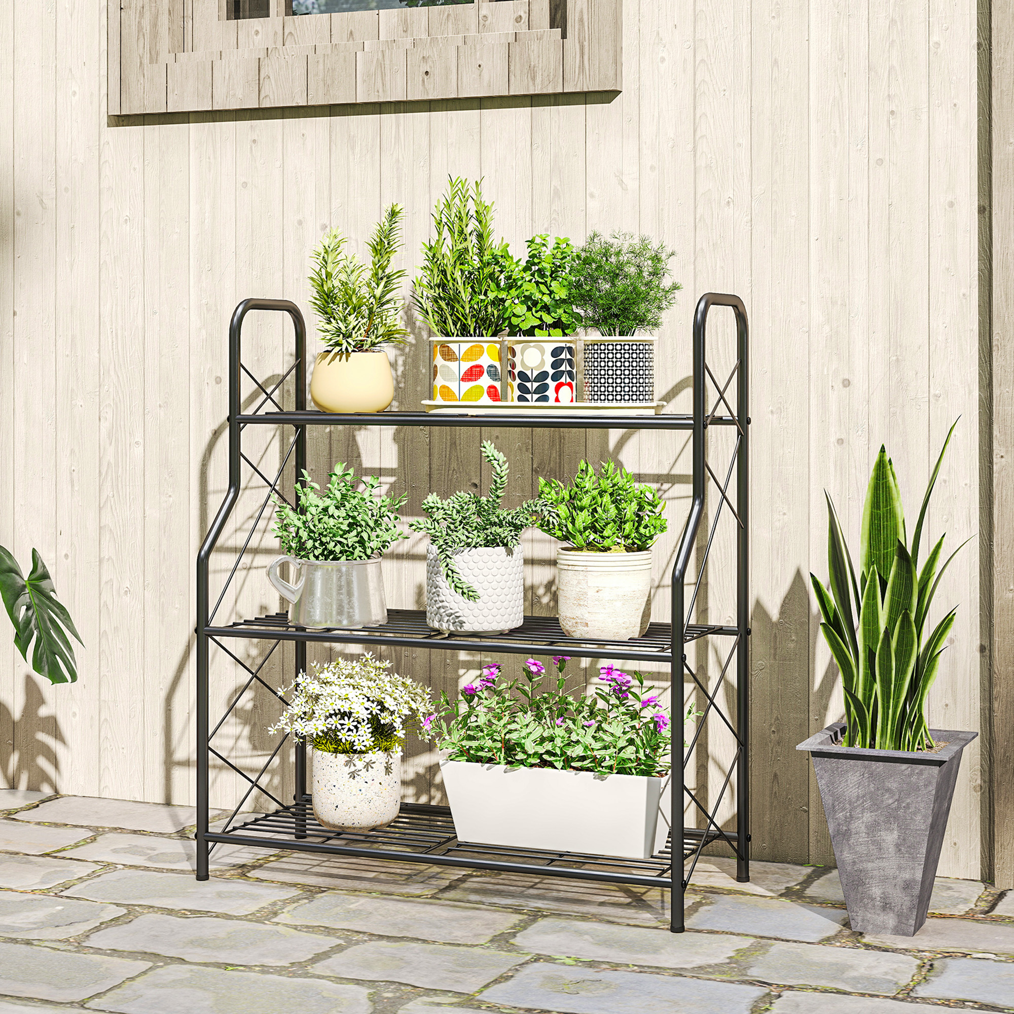 Un estante negro para plantas con macetas frente a una pared de madera. Hay adoquines delante.