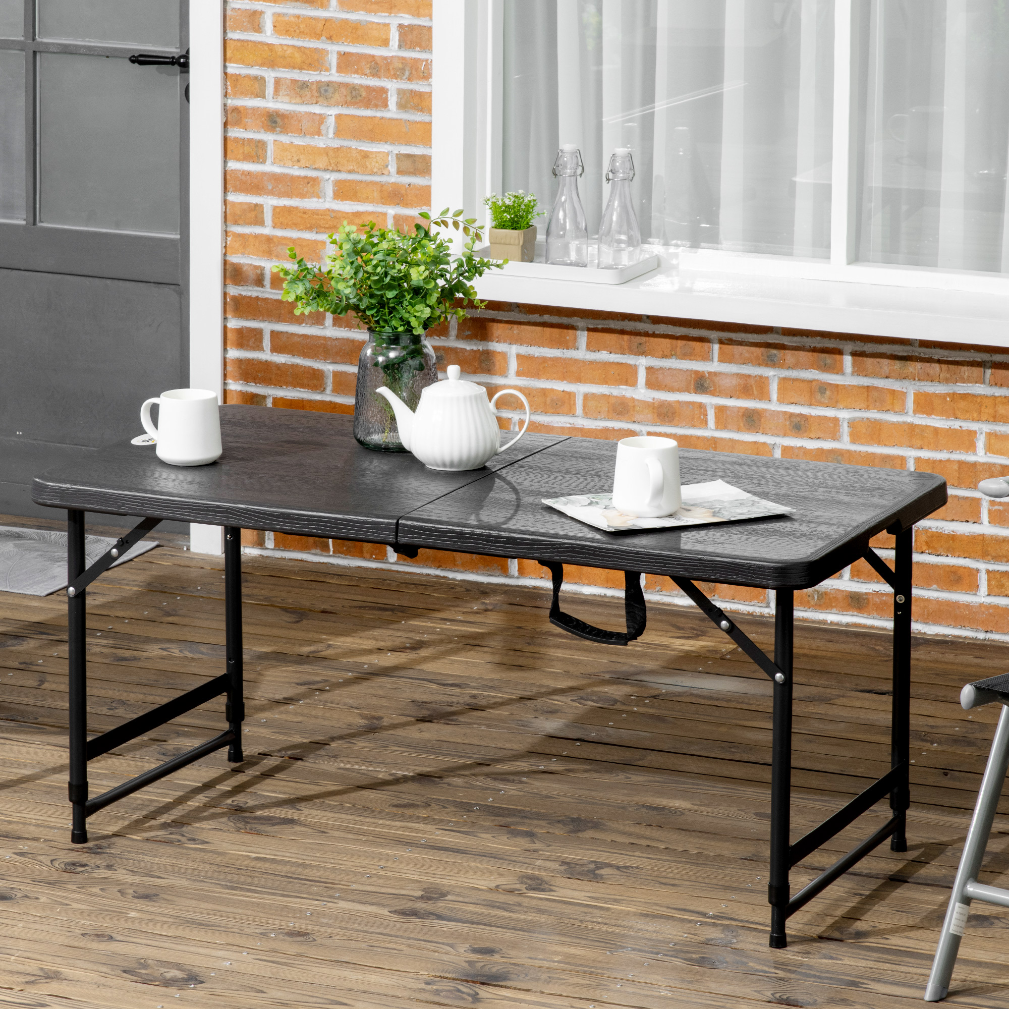 Una mesa plegable negra con dos tazas blancas, una tetera y una planta.