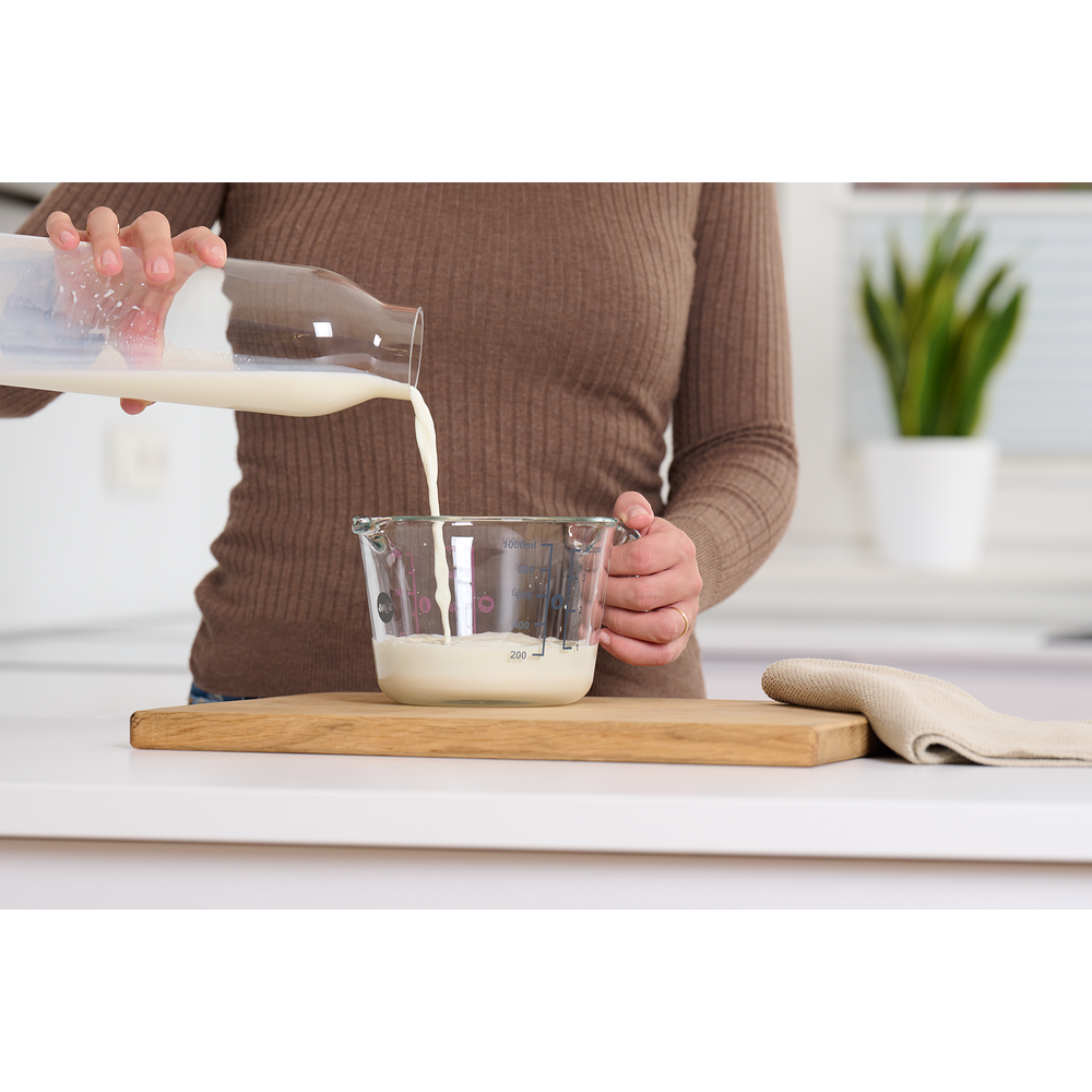 Milch wird aus einer Glasflasche in einen Messbecher gegossen.