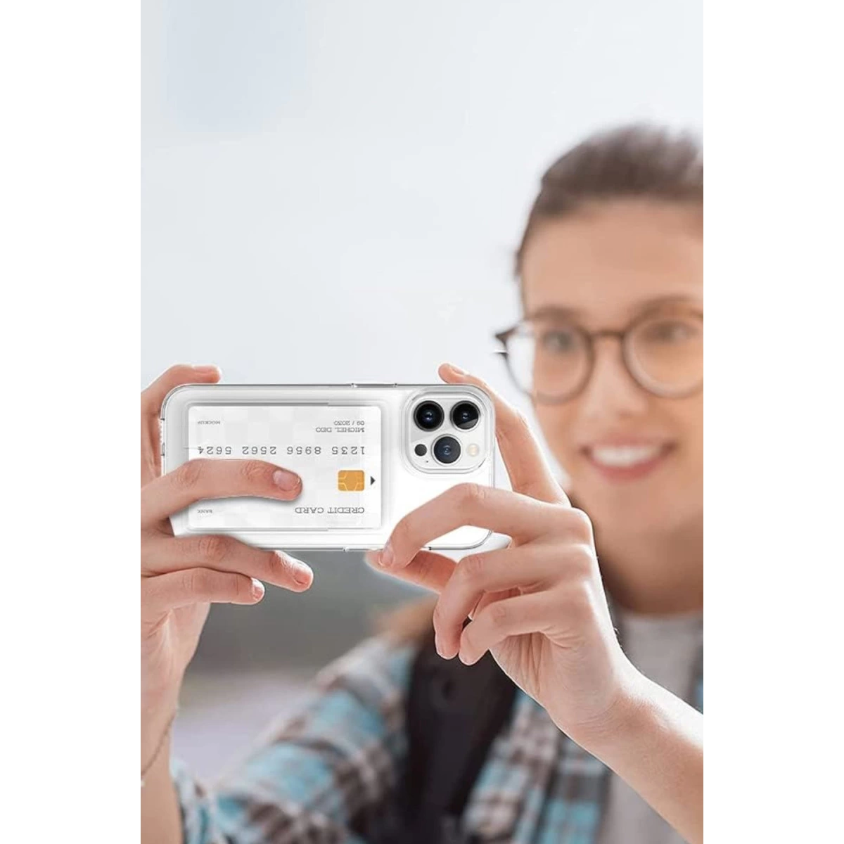 Bir kadın kredi kartı içeren şeffaf kılıflı bir akıllı telefon tutuyor.
