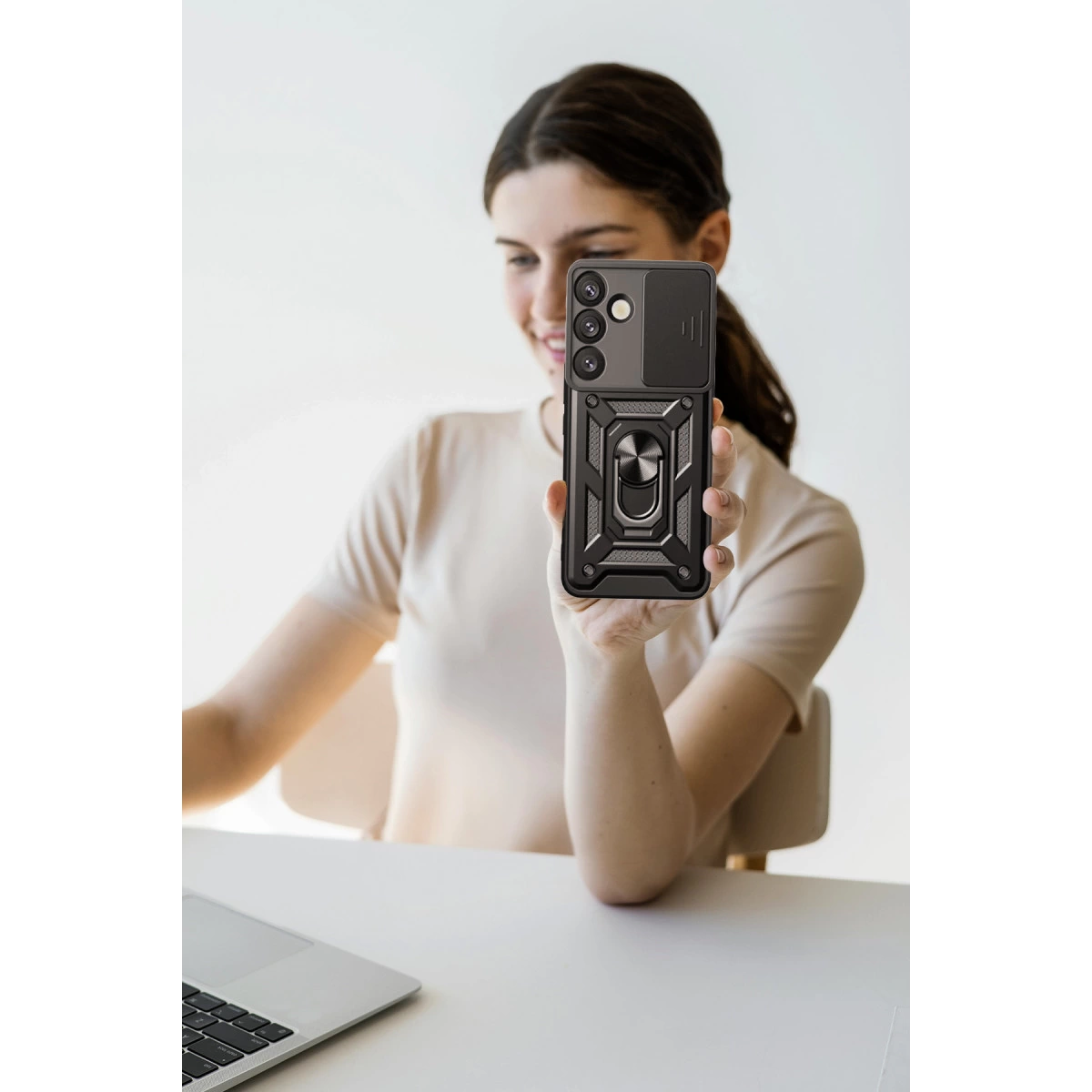 Bir kadın, önünde koruyucu kılıflı ve halka tutuculu siyah bir telefon tutuyor.