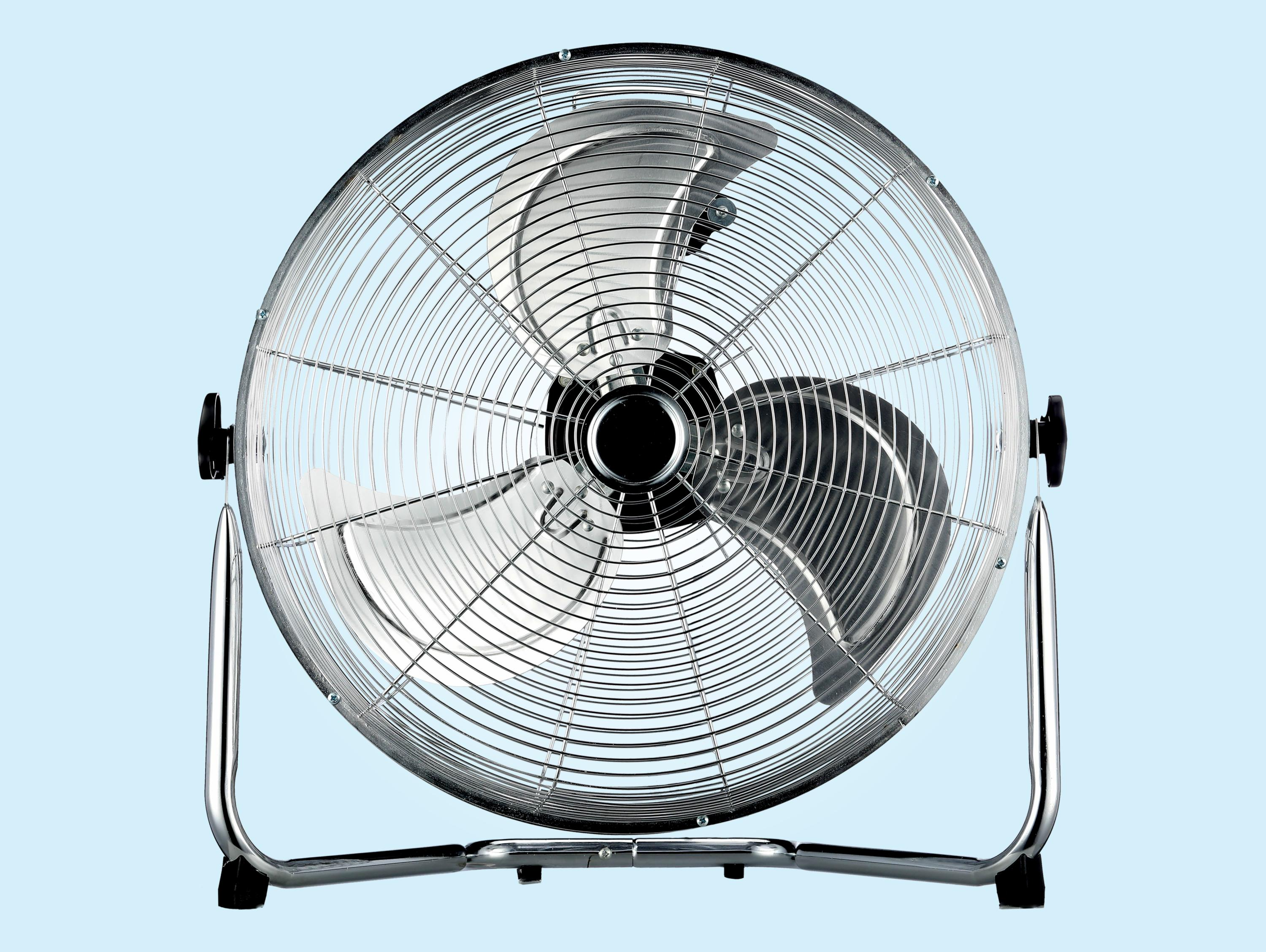 Un ventilador de pie plateado con tres aspas sobre fondo azul claro.