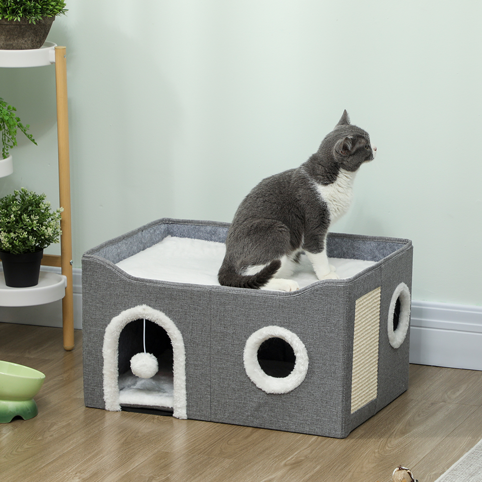 Gato gris y blanco sentado en una casa para gatos gris con borde blanco y dos entradas.