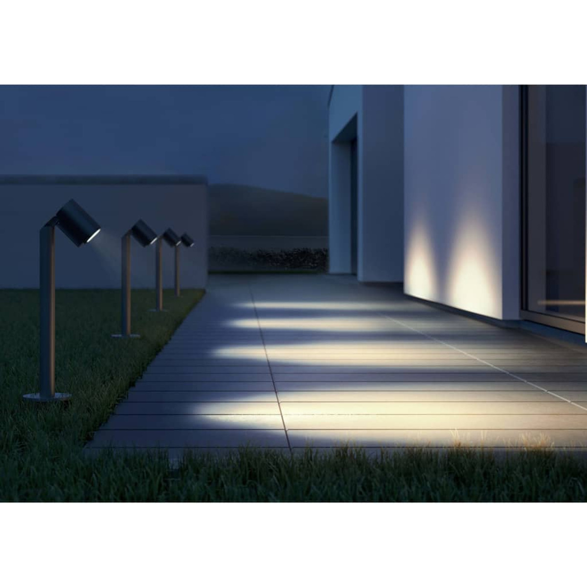 Modernas luces exteriores iluminan un camino junto a una casa por la noche.