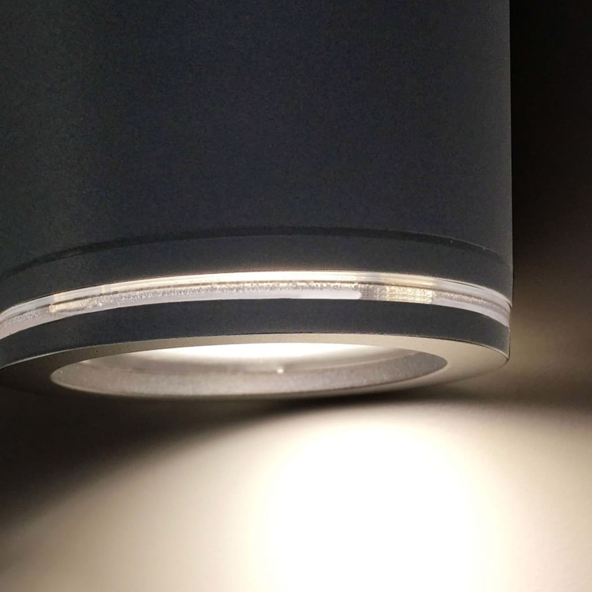 Una lámpara cilíndrica oscura con borde plateado, iluminada por LEDs brillantes.