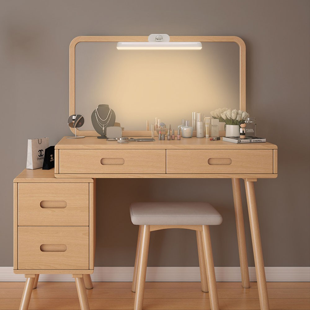 Un tocador de madera clara con espejo, cajones, joyas y cosméticos.