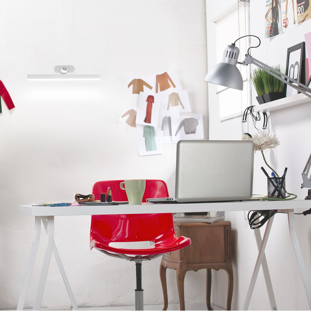 Una silla roja delante de un escritorio con portátil, taza y lápiz labial.