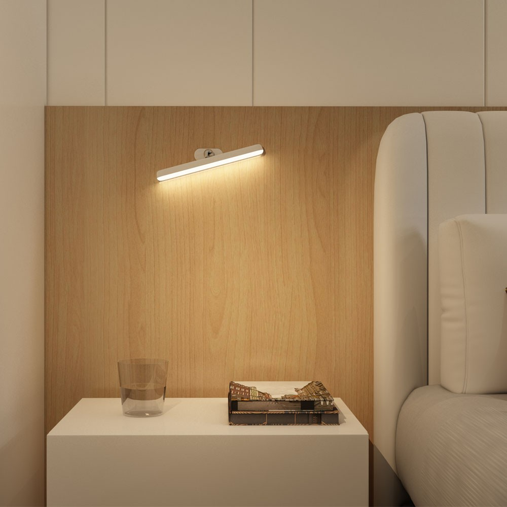 Una mesita de noche con un vaso de agua y un libro, iluminada por una lámpara de pared.