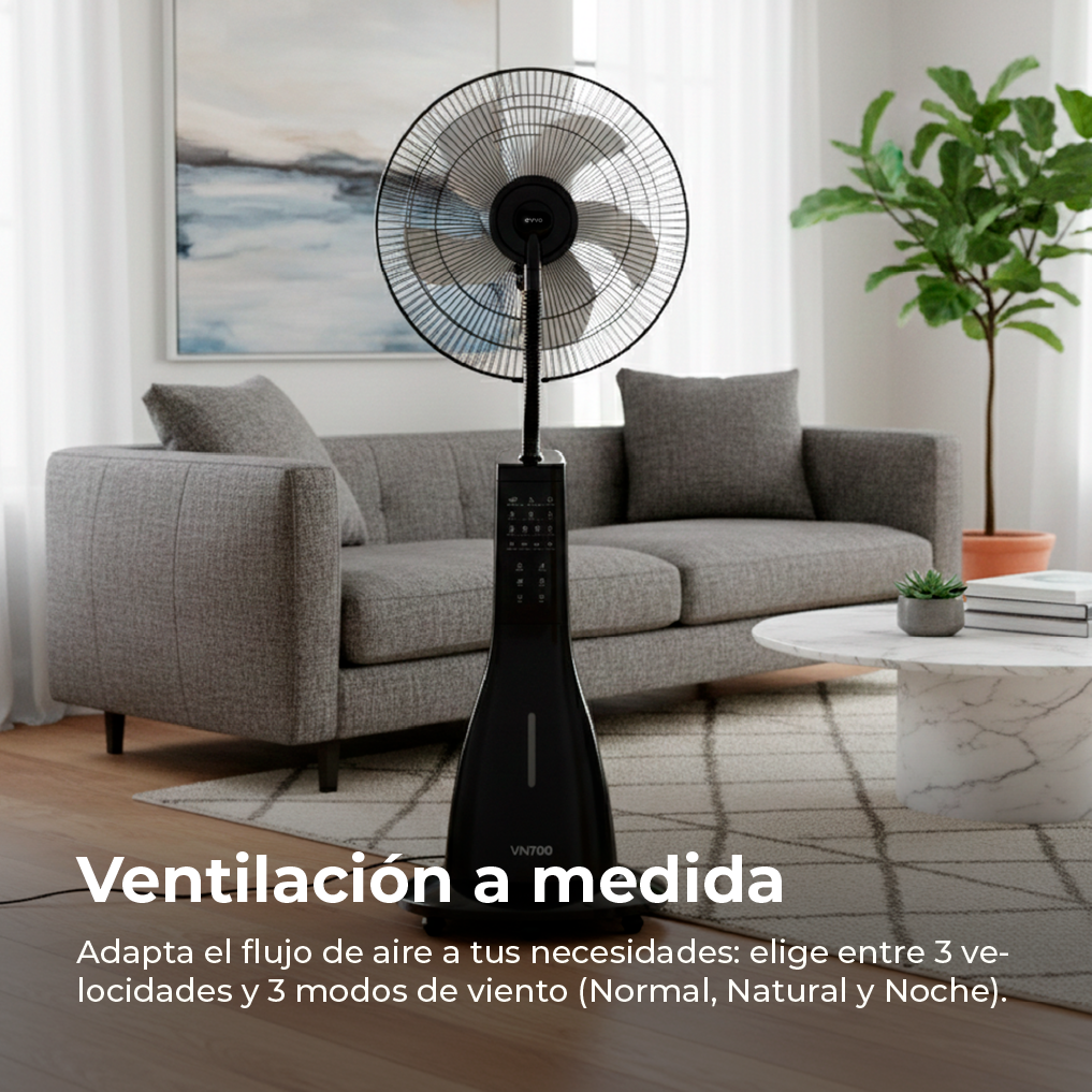 Un ventilador negro se alza delante de un sofá gris en una sala.