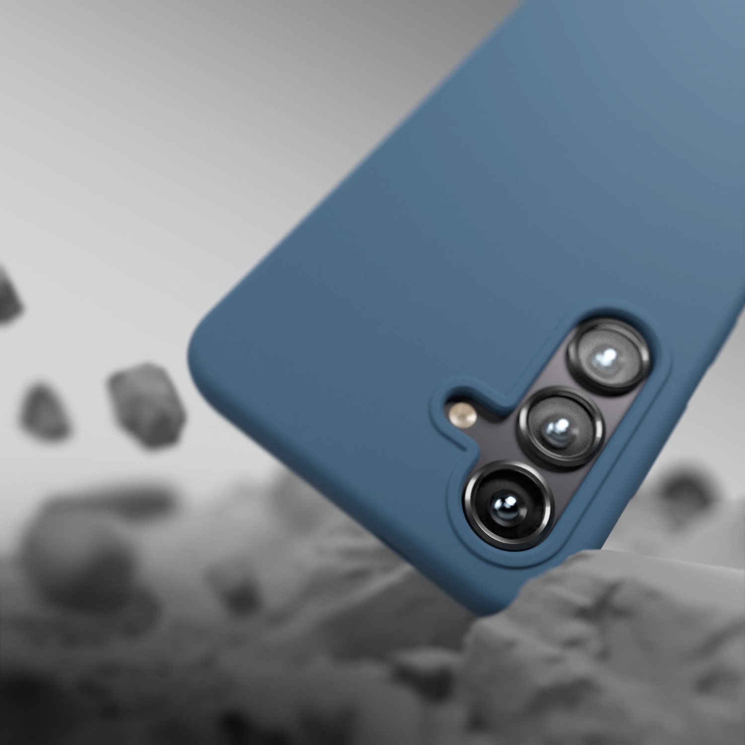 Una custodia blu per telefono con tre fotocamere cade sulle rocce.