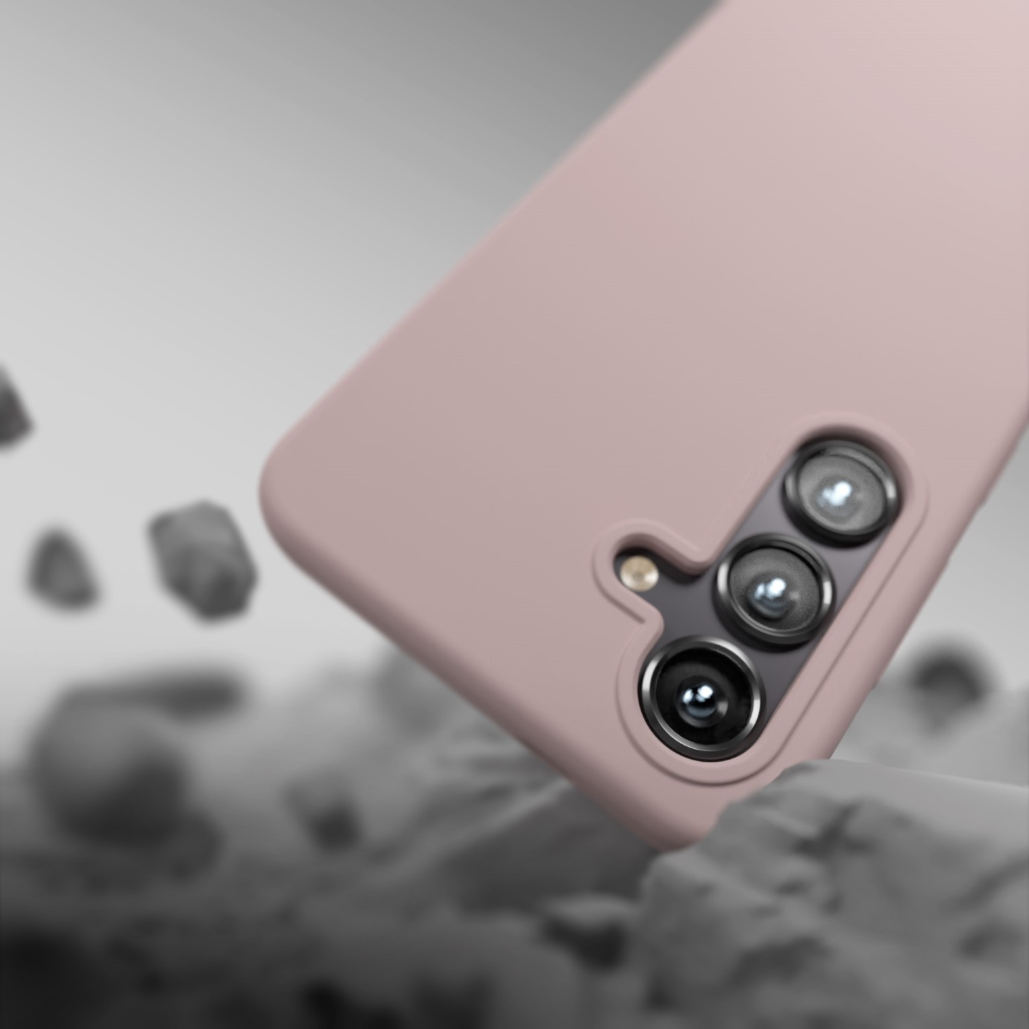 Una cover rosa per telefono con tre fotocamere cade su rocce grigie.