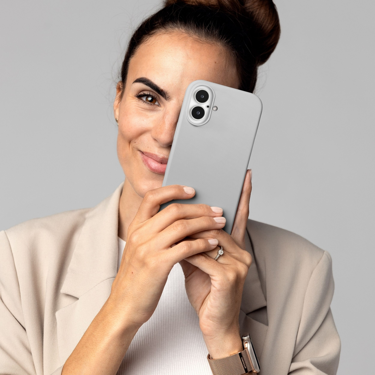Frau mit Dutt hält ein graues Handy vor ihr Gesicht, trägt beige Jacke.