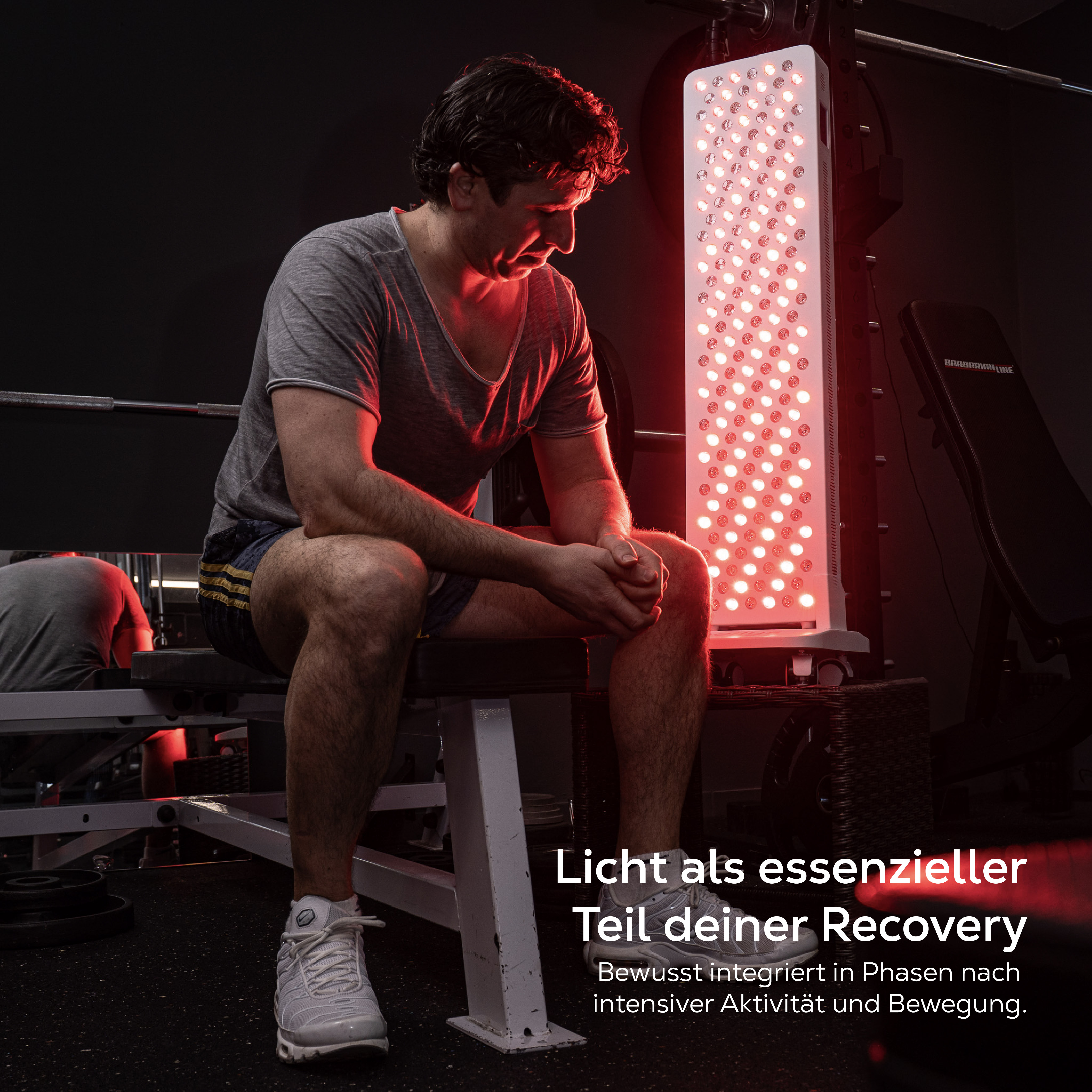 Mann sitzt auf einer Bank vor einer roten Lichttherapie-Platte im Fitnessstudio.
