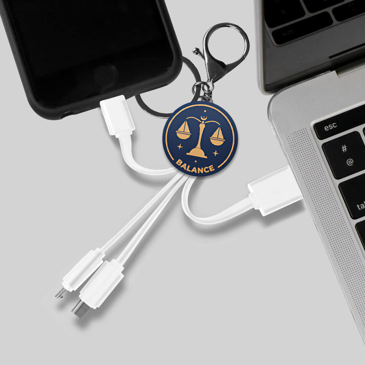Un portachiavi con simbolo di bilancia e cavi di ricarica collegati a uno smartphone e un laptop.